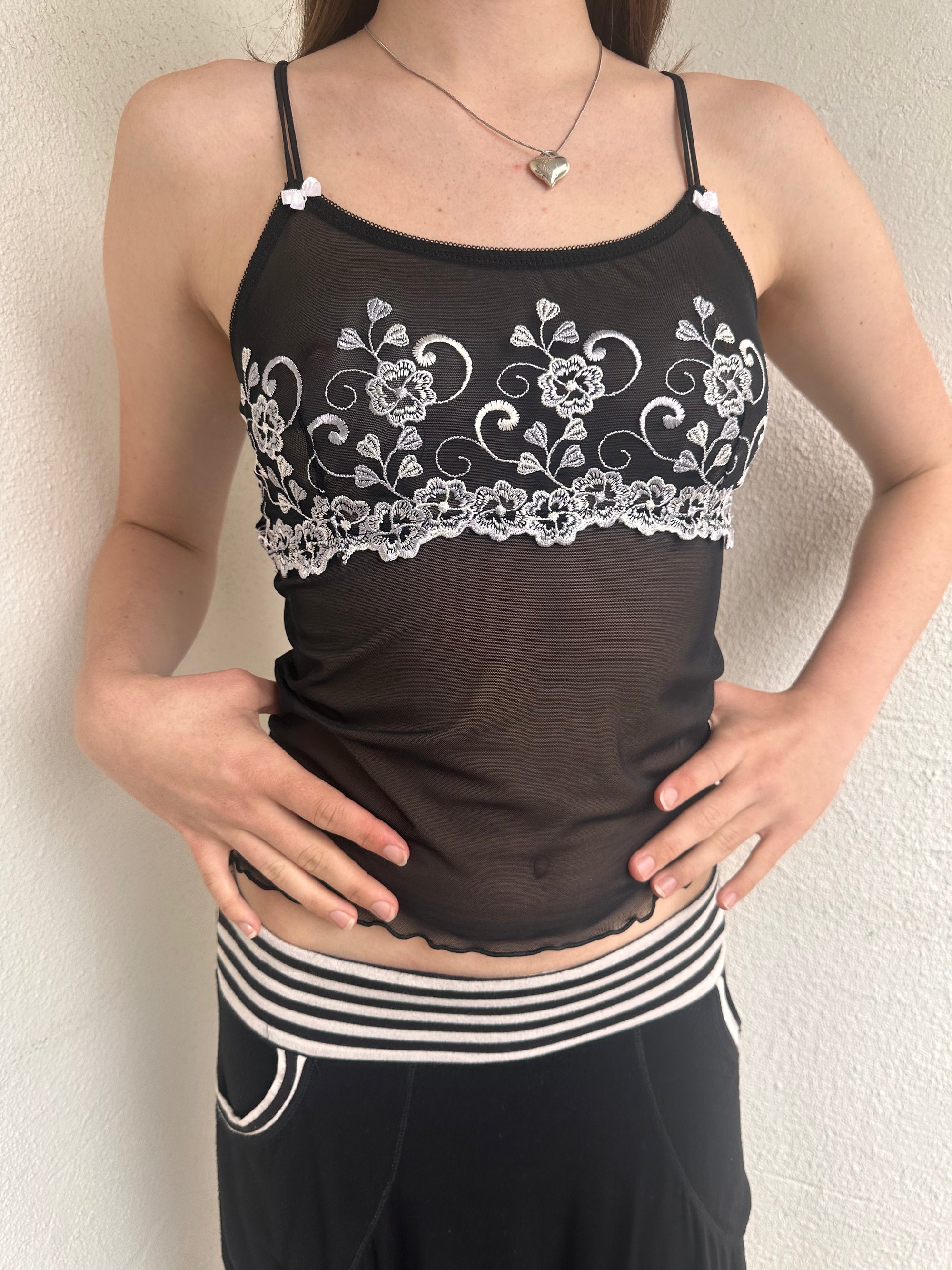 Woman wearing a Y2K 00s Black with white floral embroidery mesh cami top 