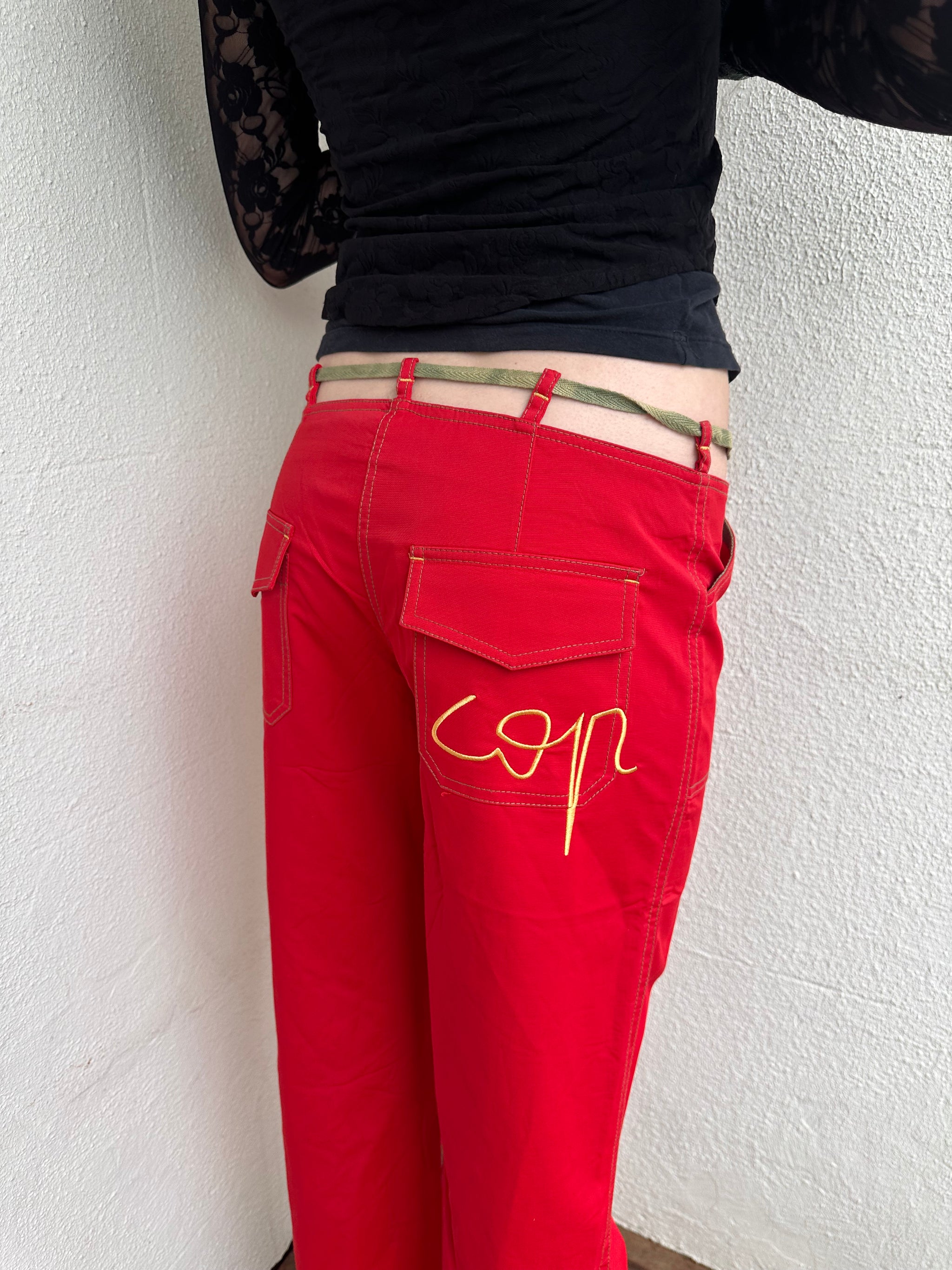 Woman wearing a Y2K 00s Cop copine red straight leg and low waited pants with cut out waistband and yellow embroidery 