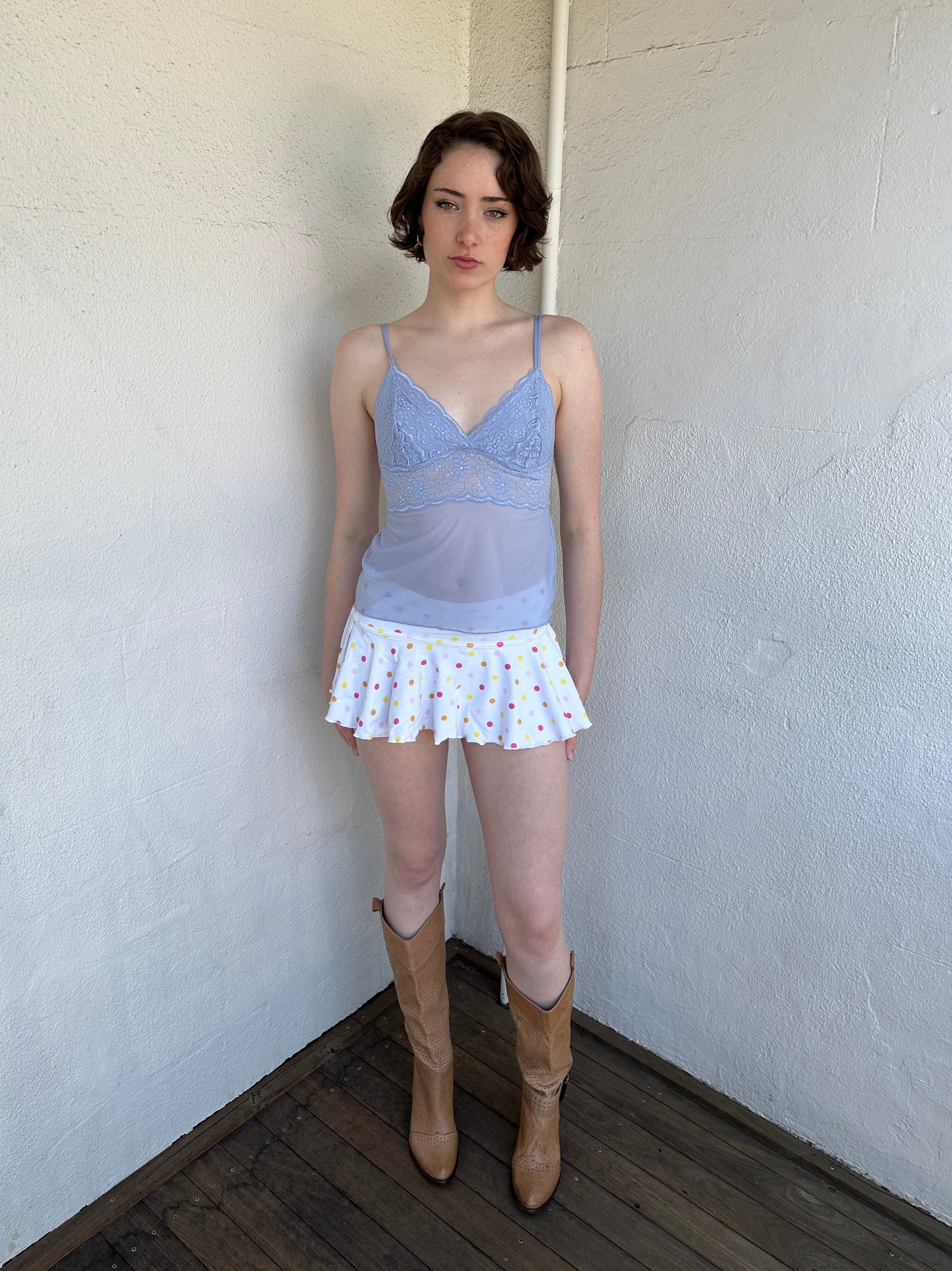 Woman Dressed in Y2K Baby blue lace cami top featuring a soft dusky blue tone with a lace bust and sheer mesh body. 