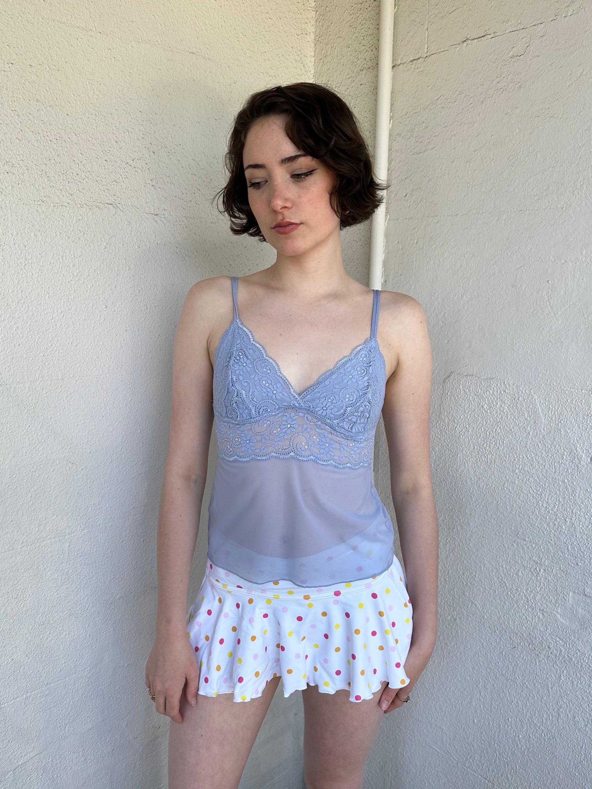 Woman Dressed in Y2K Baby blue lace cami top featuring a soft dusky blue tone with a lace bust and sheer mesh body. 