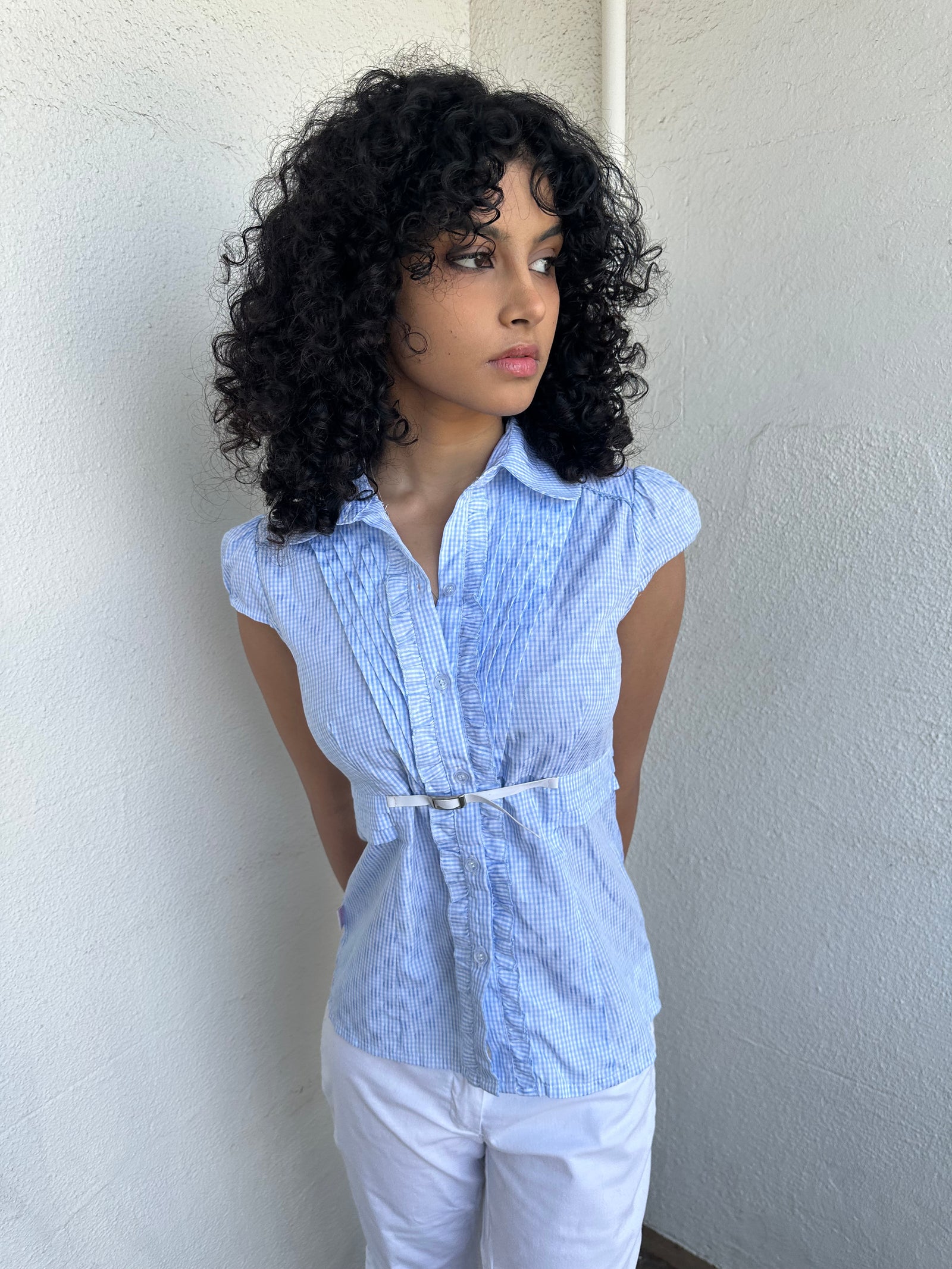 Woman wearing a Y2K 00s Baby blue gingham shirt with, featuring delicate ruffles down the front