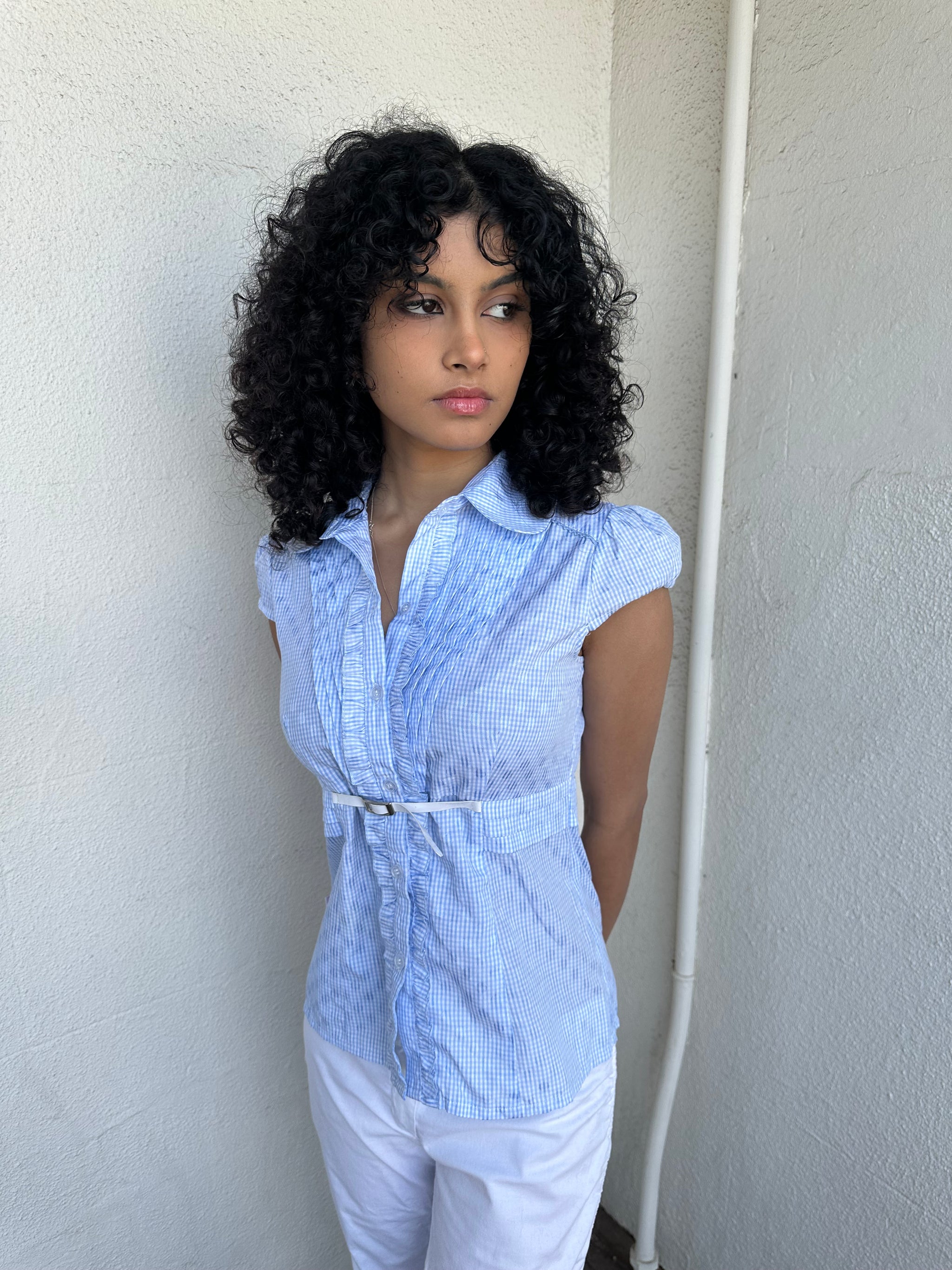 Woman wearing a Y2K 00s Baby blue gingham shirt with, featuring delicate ruffles down the front