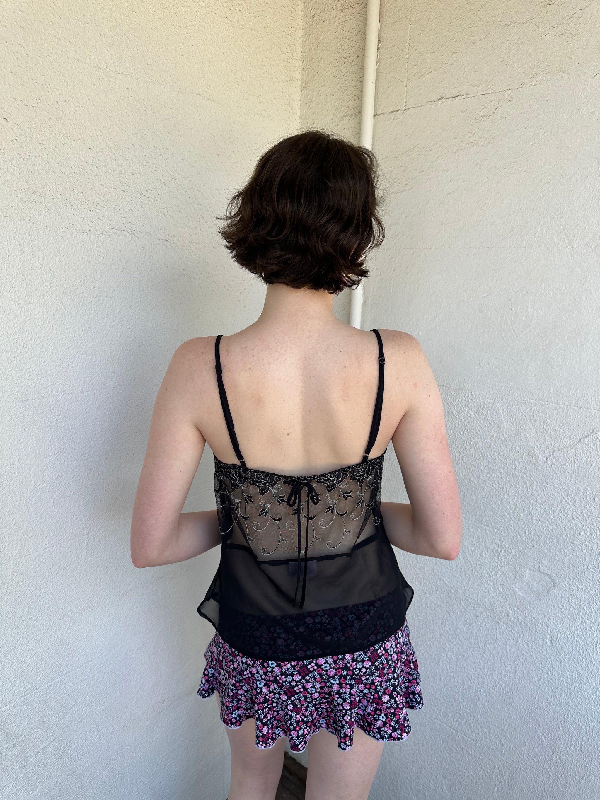 Woman Dressed in Y2K Black embroidered mesh cami top featuring a sheer bust with black and silver floral embroidery. 