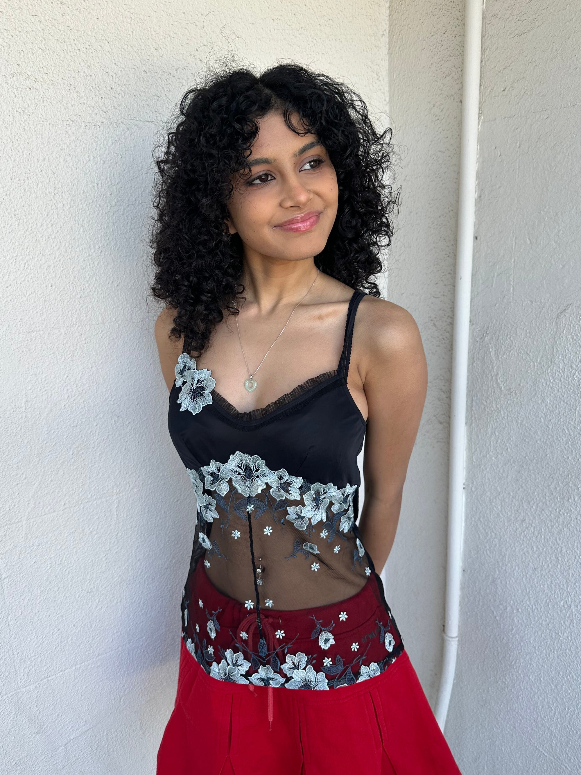 Woman wearing a Y2K 00s Black with white floral embroidery mesh cami top. Light blue floral embroidery featured 