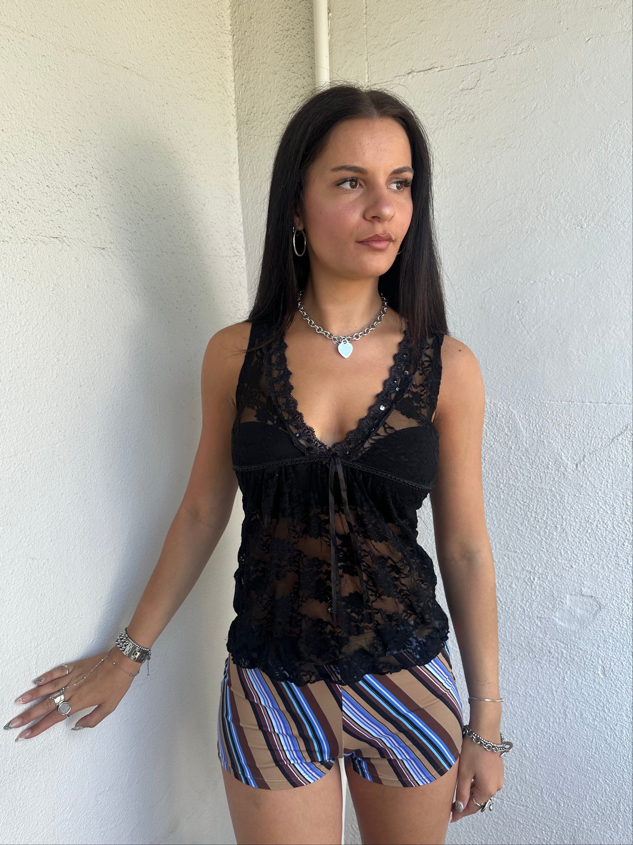 Woman Dressed in Y2K 00s Black lace ribbon detail tank top featuring a completely sheer fabric with a V-neckline and delicate ribbon bow detail at the bust.