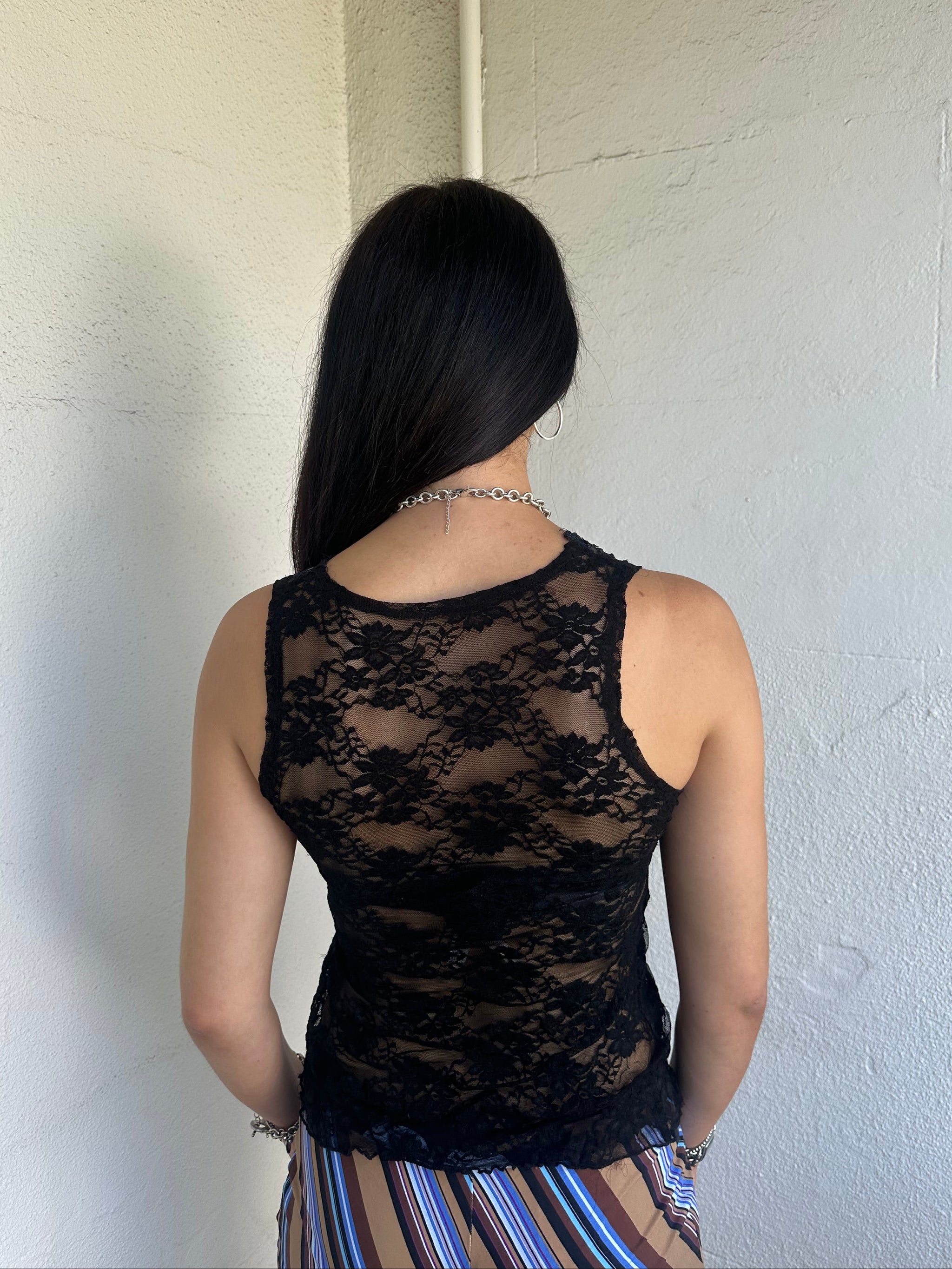Woman Dressed in Y2K 00s Black lace ribbon detail tank top featuring a completely sheer fabric with a V-neckline and delicate ribbon bow detail at the bust.