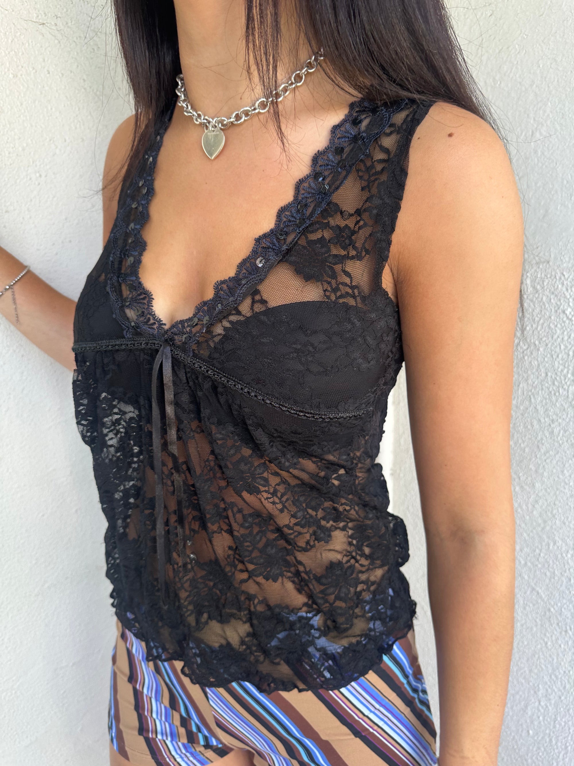 Woman Dressed in Y2K 00s Black lace ribbon detail tank top featuring a completely sheer fabric with a V-neckline and delicate ribbon bow detail at the bust.