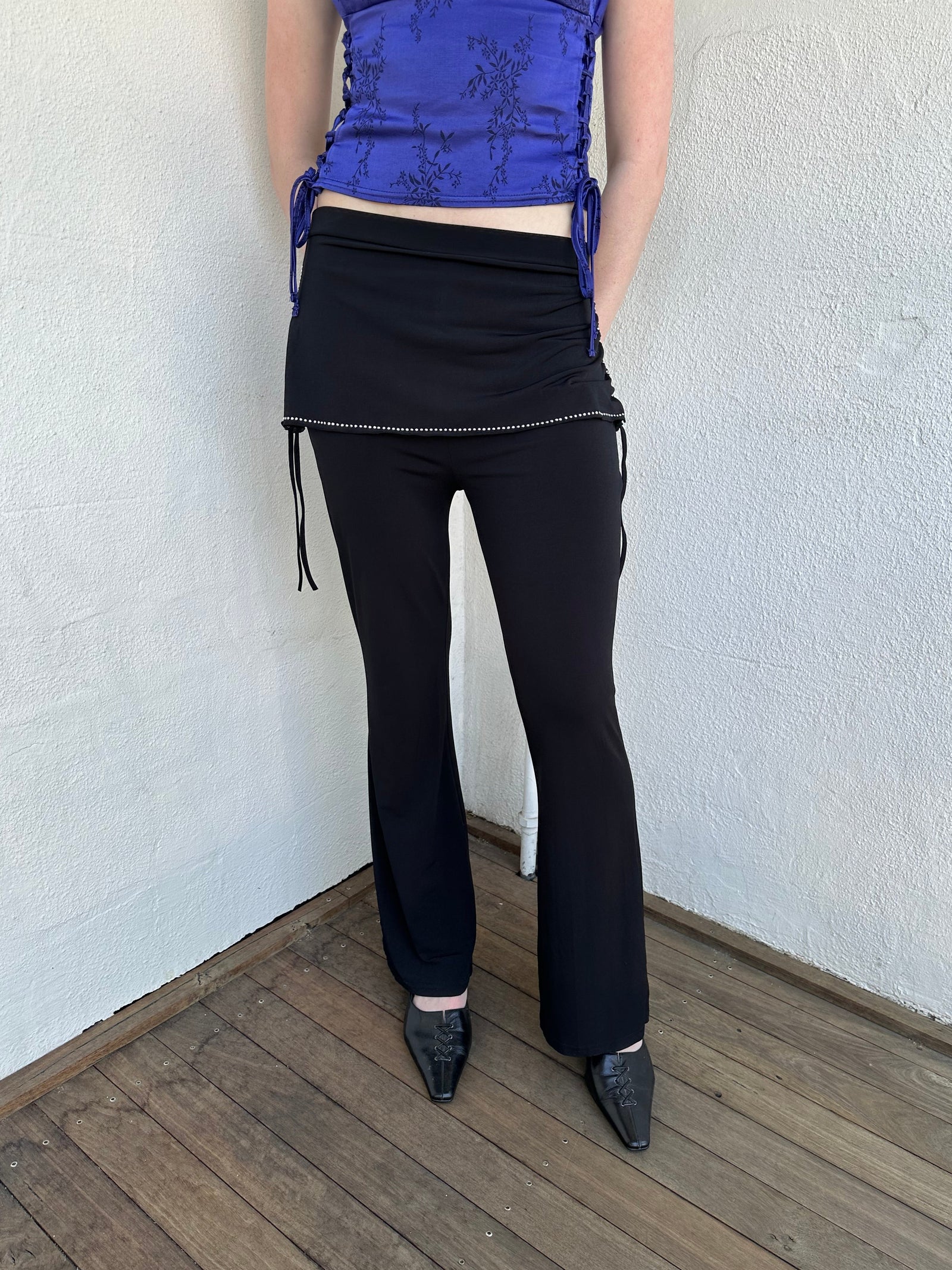 Woman Dressed in Y2K Black rhinestone detail skirt pants featuring a mini skirt attached over flared pants. 