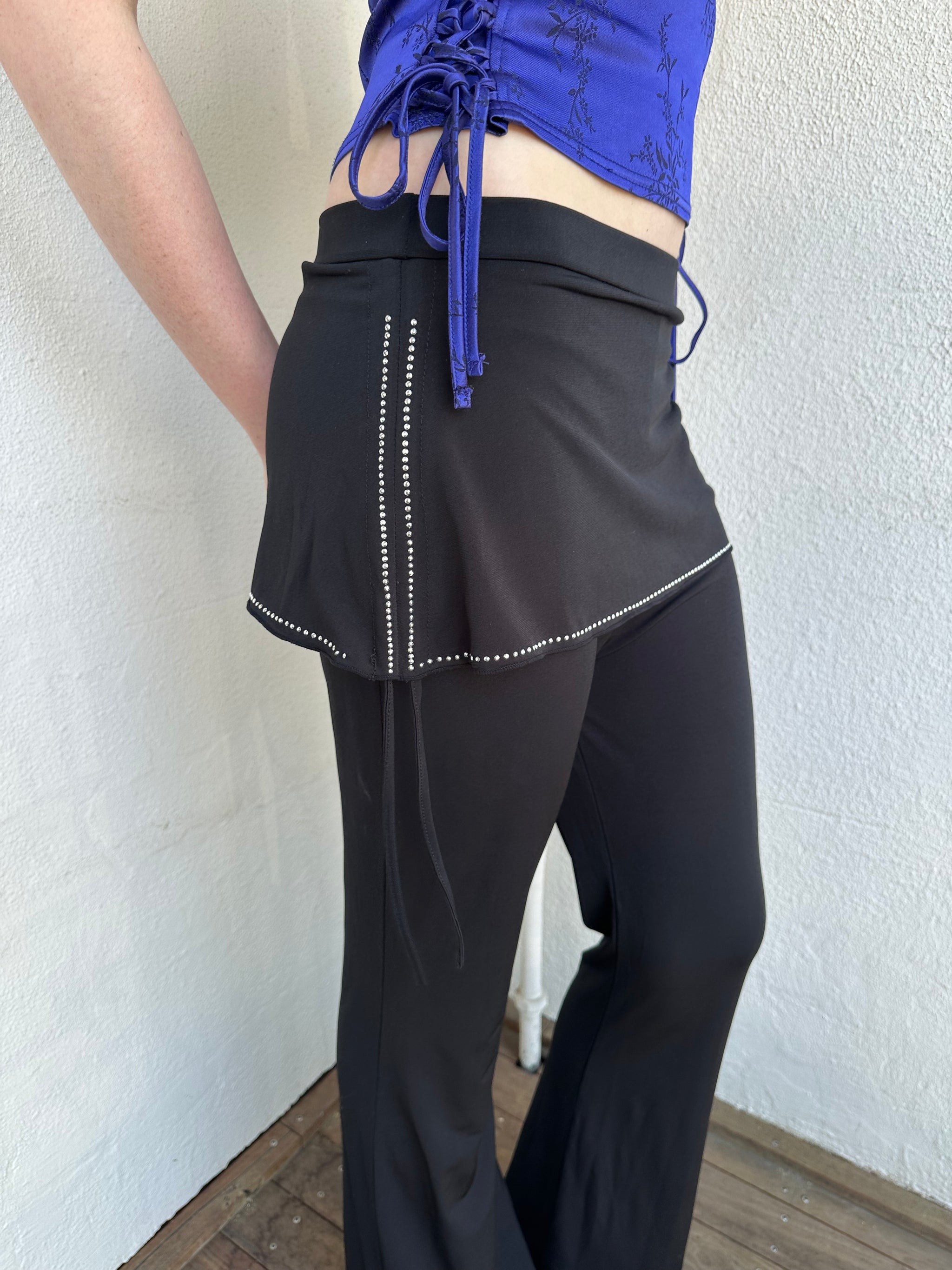 Woman Dressed in Y2K Black rhinestone detail skirt pants featuring a mini skirt attached over flared pants. 