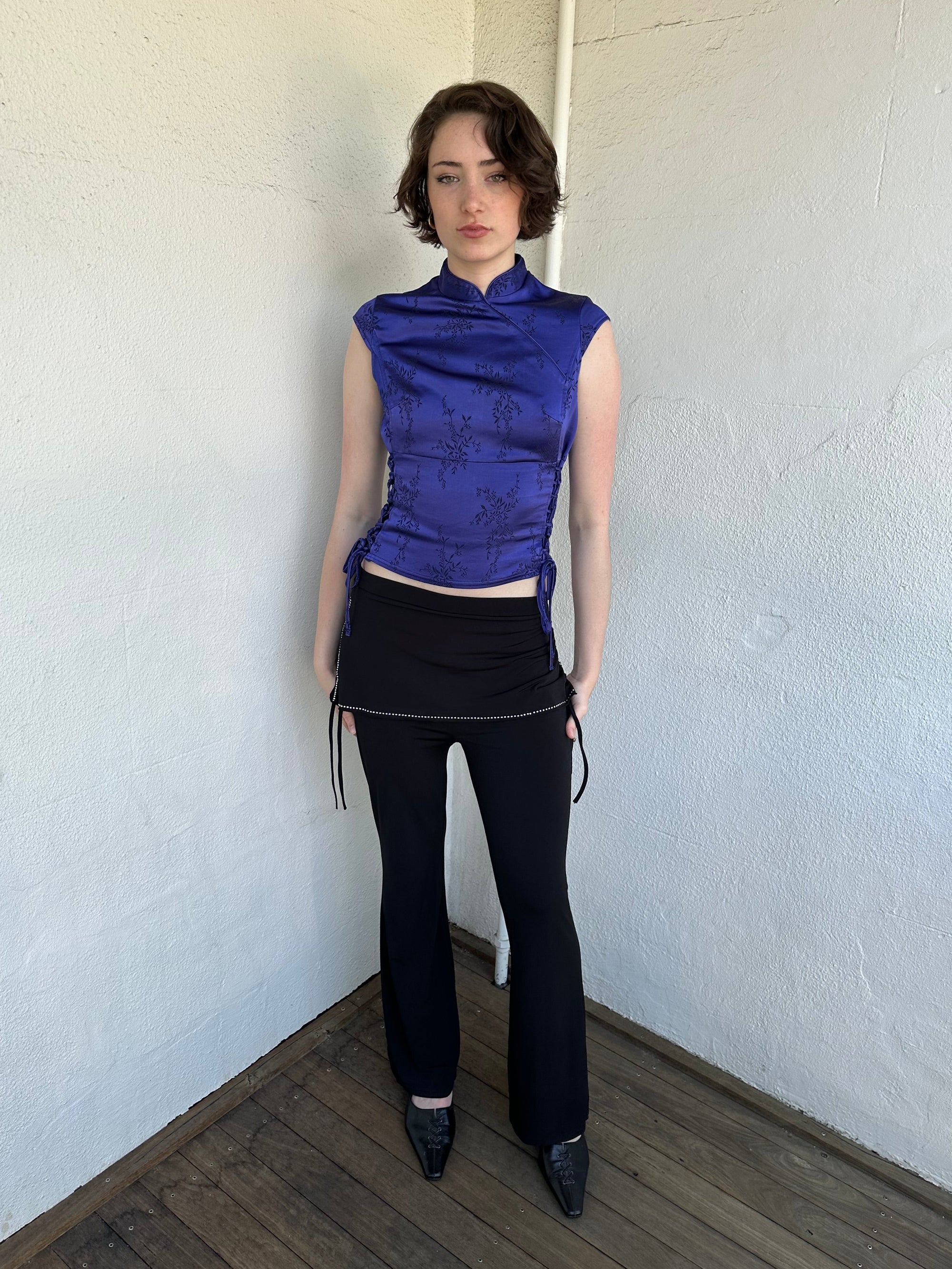 Woman Dressed in Y2K Black rhinestone detail skirt pants featuring a mini skirt attached over flared pants. 
