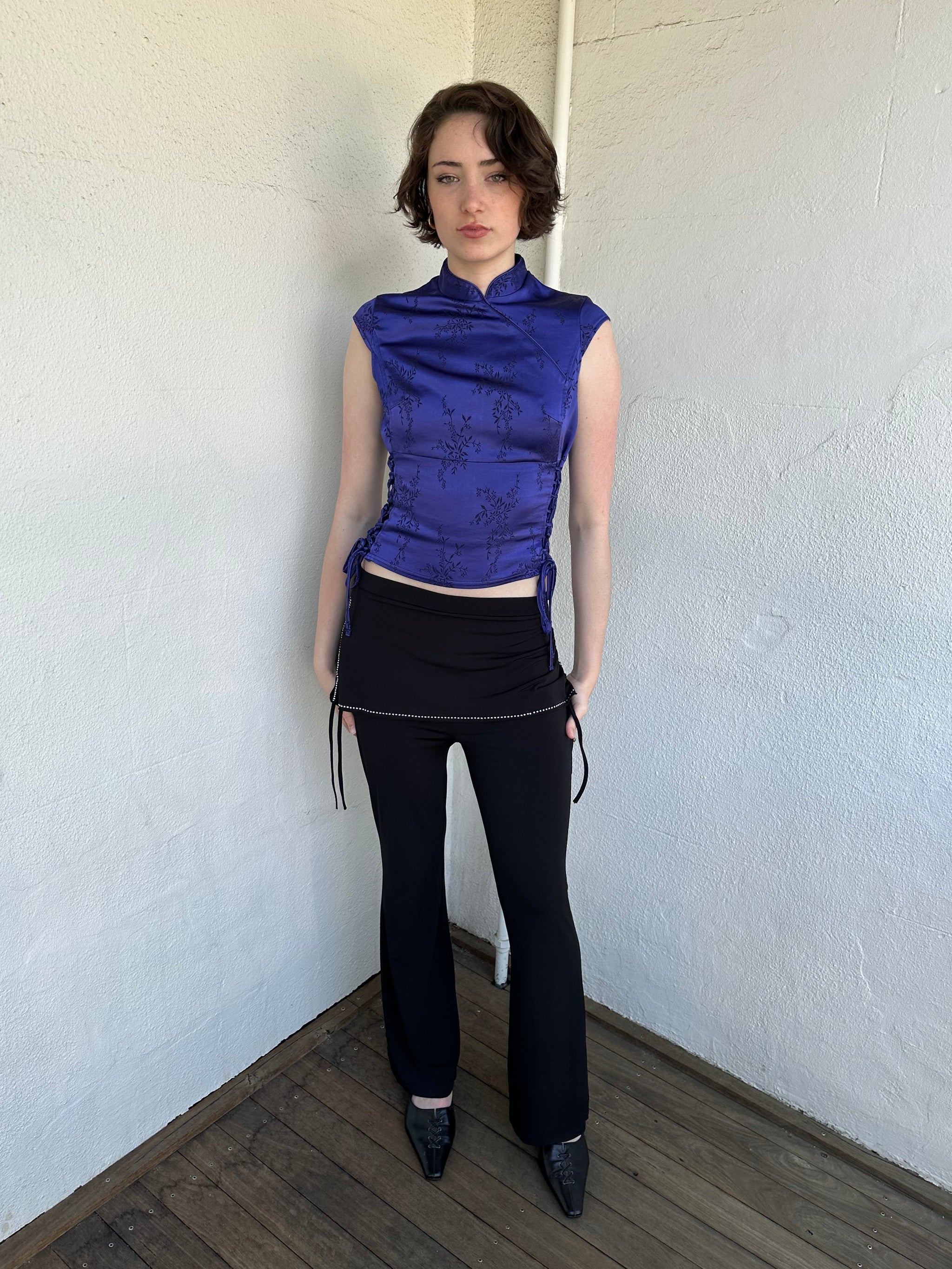 Woman Dressed in Y2K Black rhinestone detail skirt pants featuring a mini skirt attached over flared pants. 