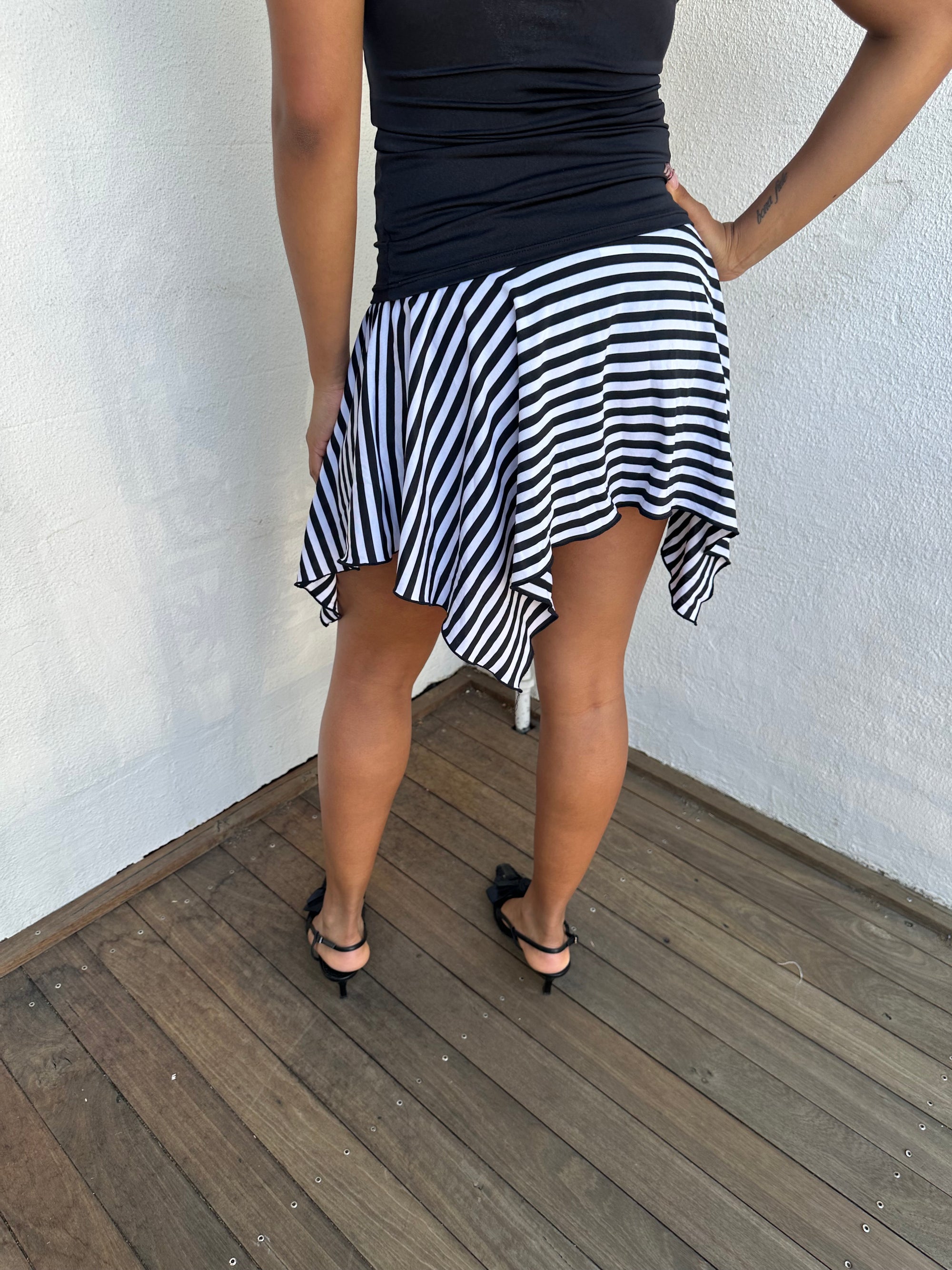 Woman Dressed in Y2K 00s Black and white stripe asymmetric skirt featuring a bold striped pattern and a hanky hem for a playful, flared silhouette.
