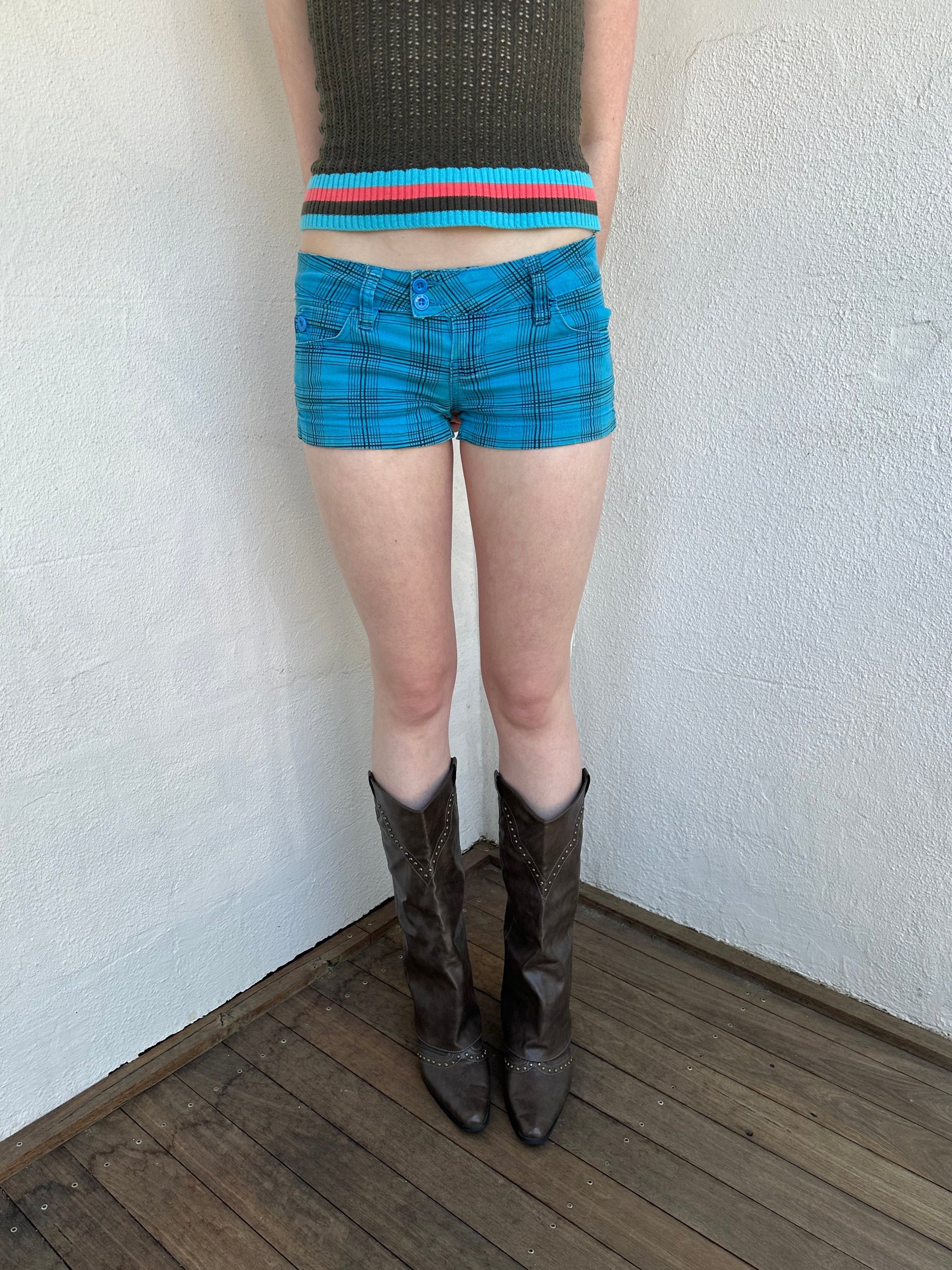 Woman Dressed in Y2K Blue and black plaid shorts featuring a bright blue base with black plaid detailing.