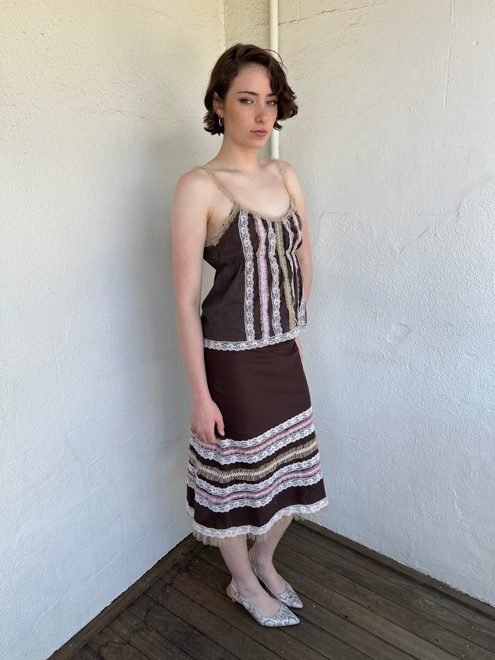 Woman Dressed in Y2K Brown and pink lace trim two piece set featuring a cami top and matching skirt detailed with cream lace and tulle trim throughout.