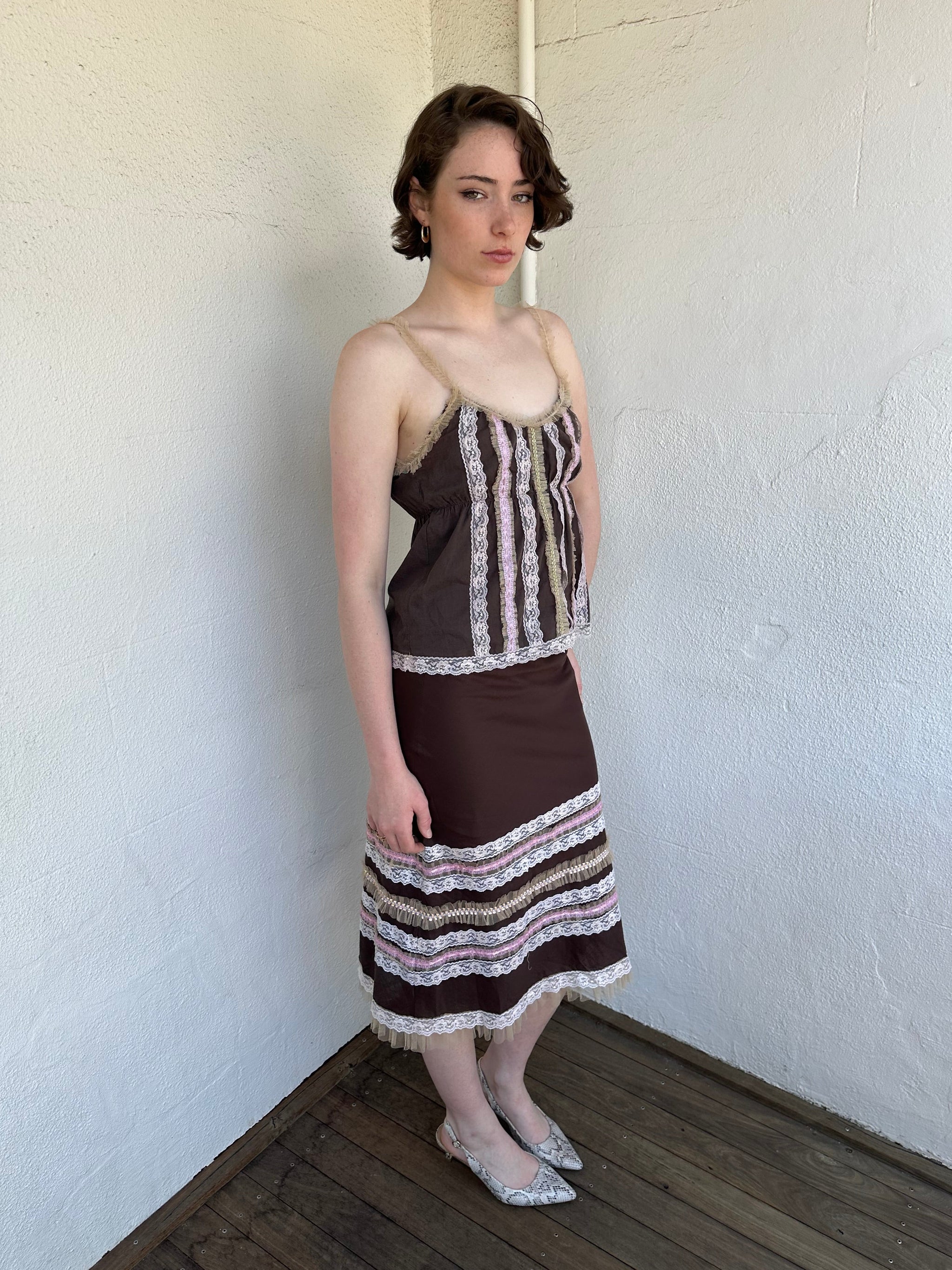 Woman Dressed in Y2K Brown and pink lace trim two piece set featuring a cami top and matching skirt detailed with cream lace and tulle trim throughout.