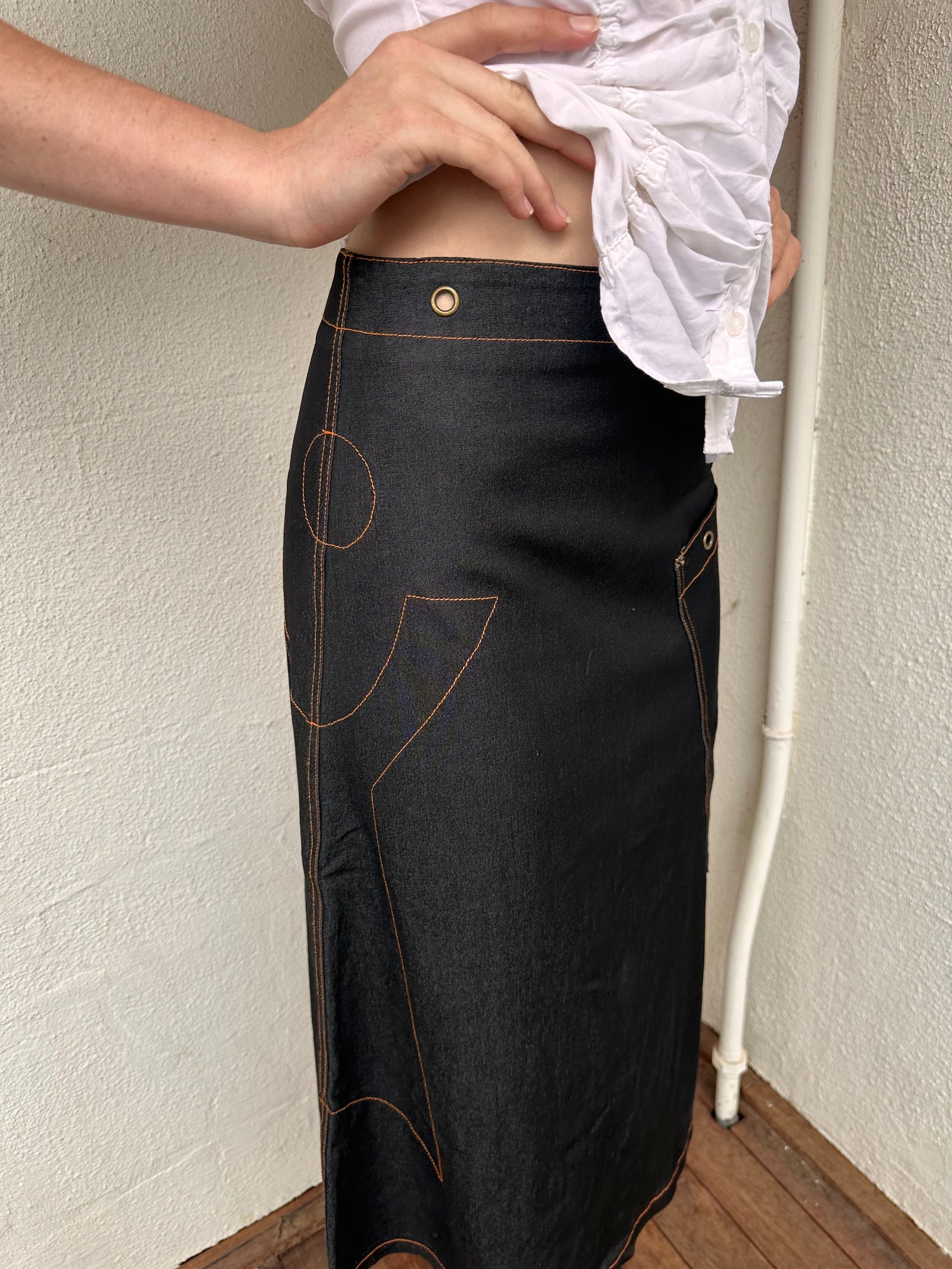 Woman wearing a Y2K 00s Cop Copine black maxi skirt stands out with bold orange contrast stitching and statement grommet details