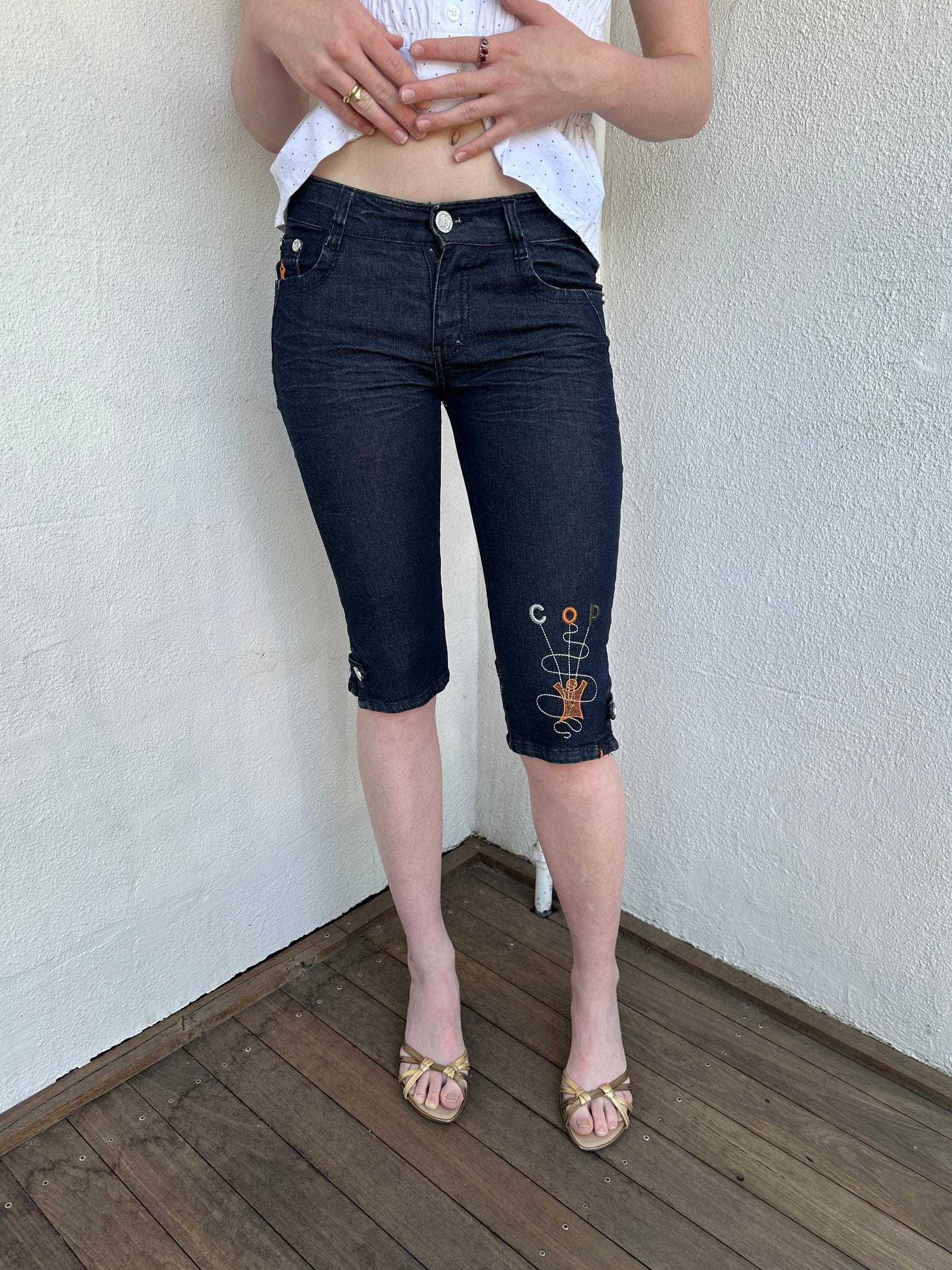 Woman Dressed in Y2K Cop Copine embroidered denim capris featuring dark denim with iconic orange and white Cop Copine logo embroidery.
