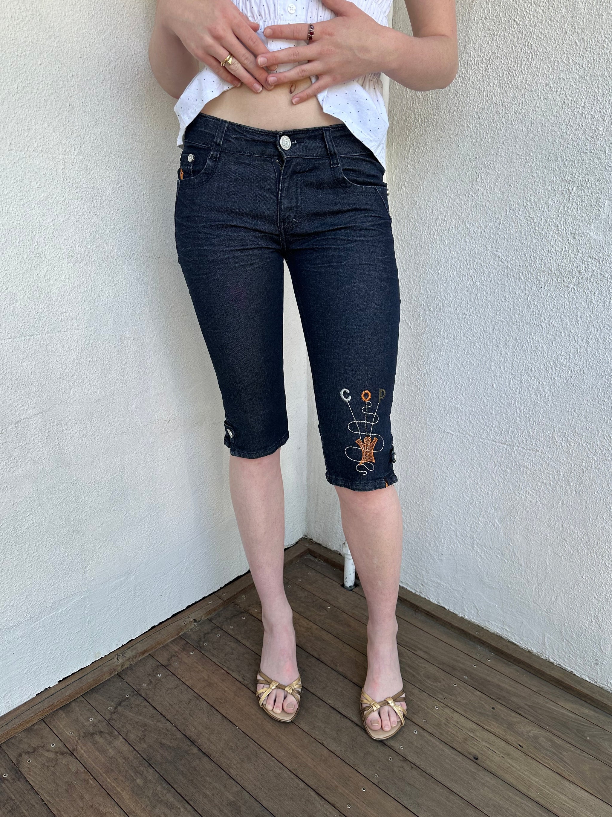 Woman Dressed in Y2K Cop Copine embroidered denim capris featuring dark denim with iconic orange and white Cop Copine logo embroidery.