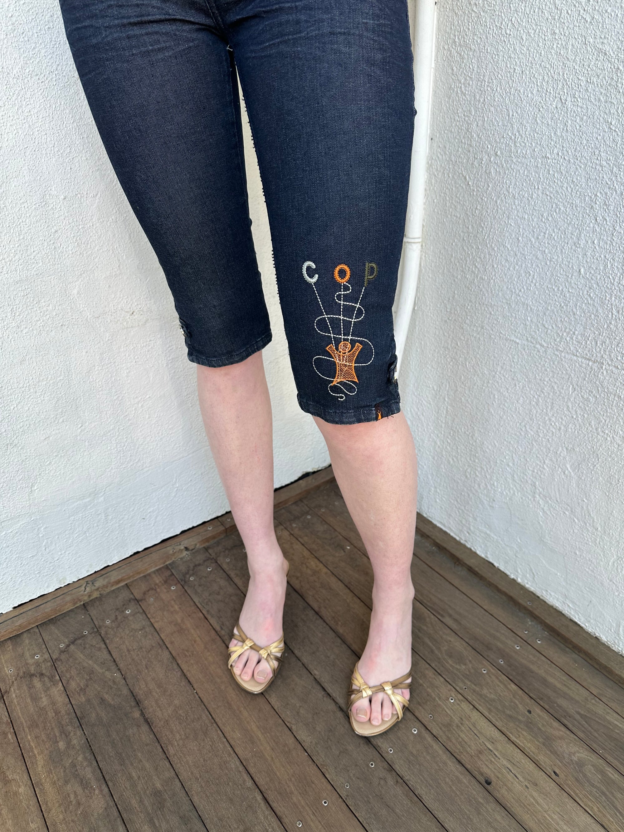 Woman Dressed in Y2K Cop Copine embroidered denim capris featuring dark denim with iconic orange and white Cop Copine logo embroidery.
