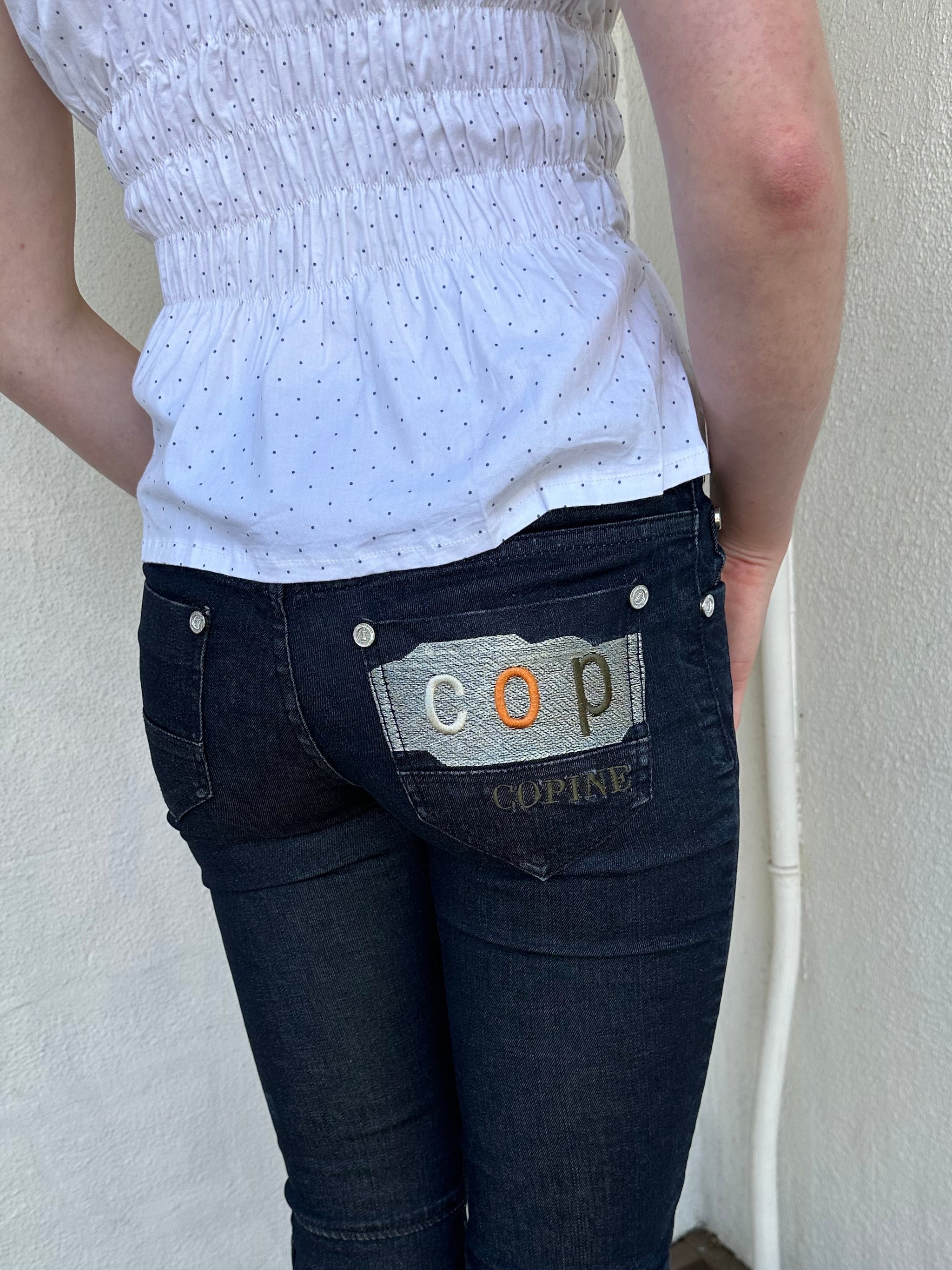 Woman Dressed in Y2K Cop Copine embroidered denim capris featuring dark denim with iconic orange and white Cop Copine logo embroidery.
