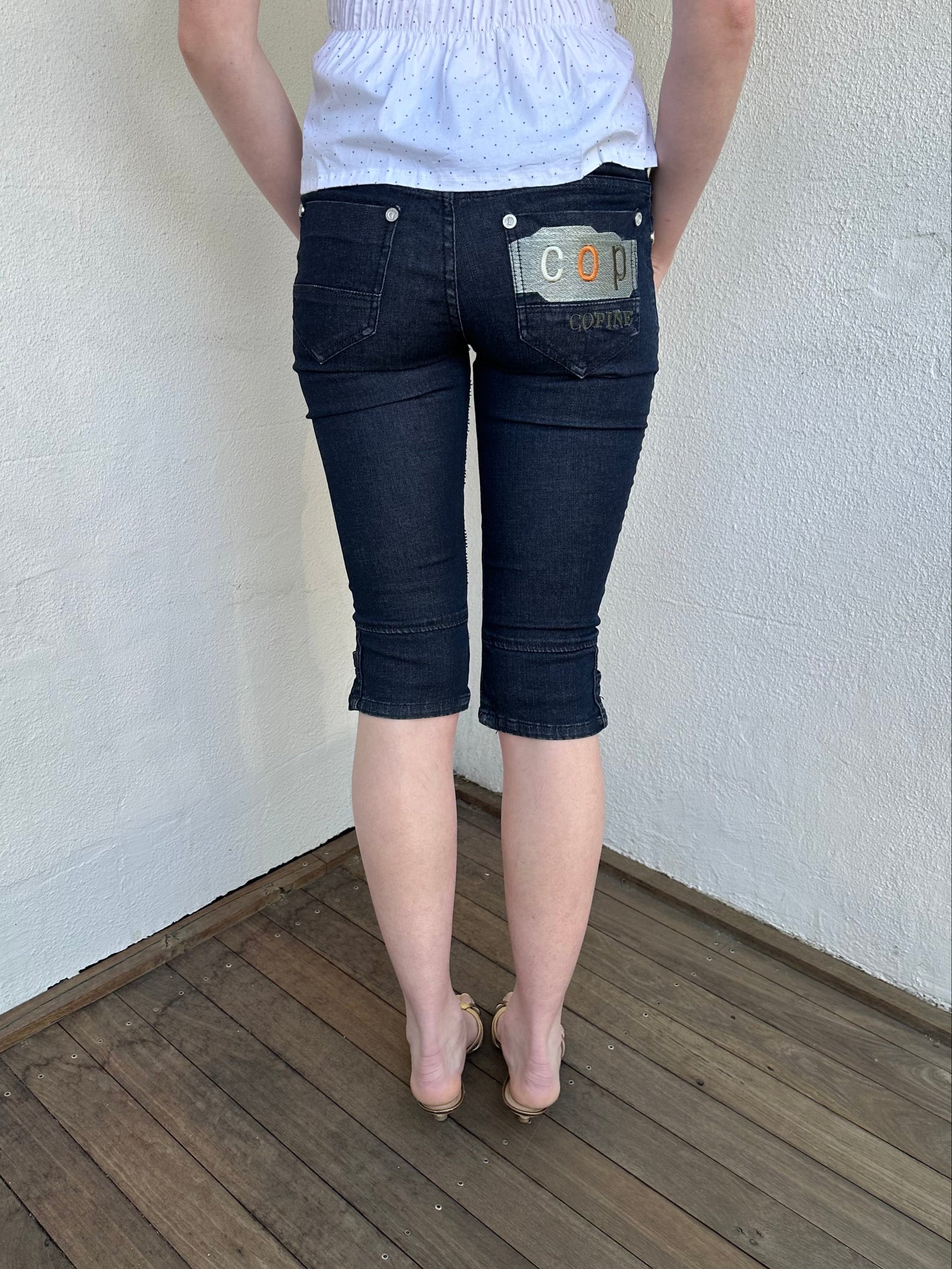 Woman Dressed in Y2K Cop Copine embroidered denim capris featuring dark denim with iconic orange and white Cop Copine logo embroidery.