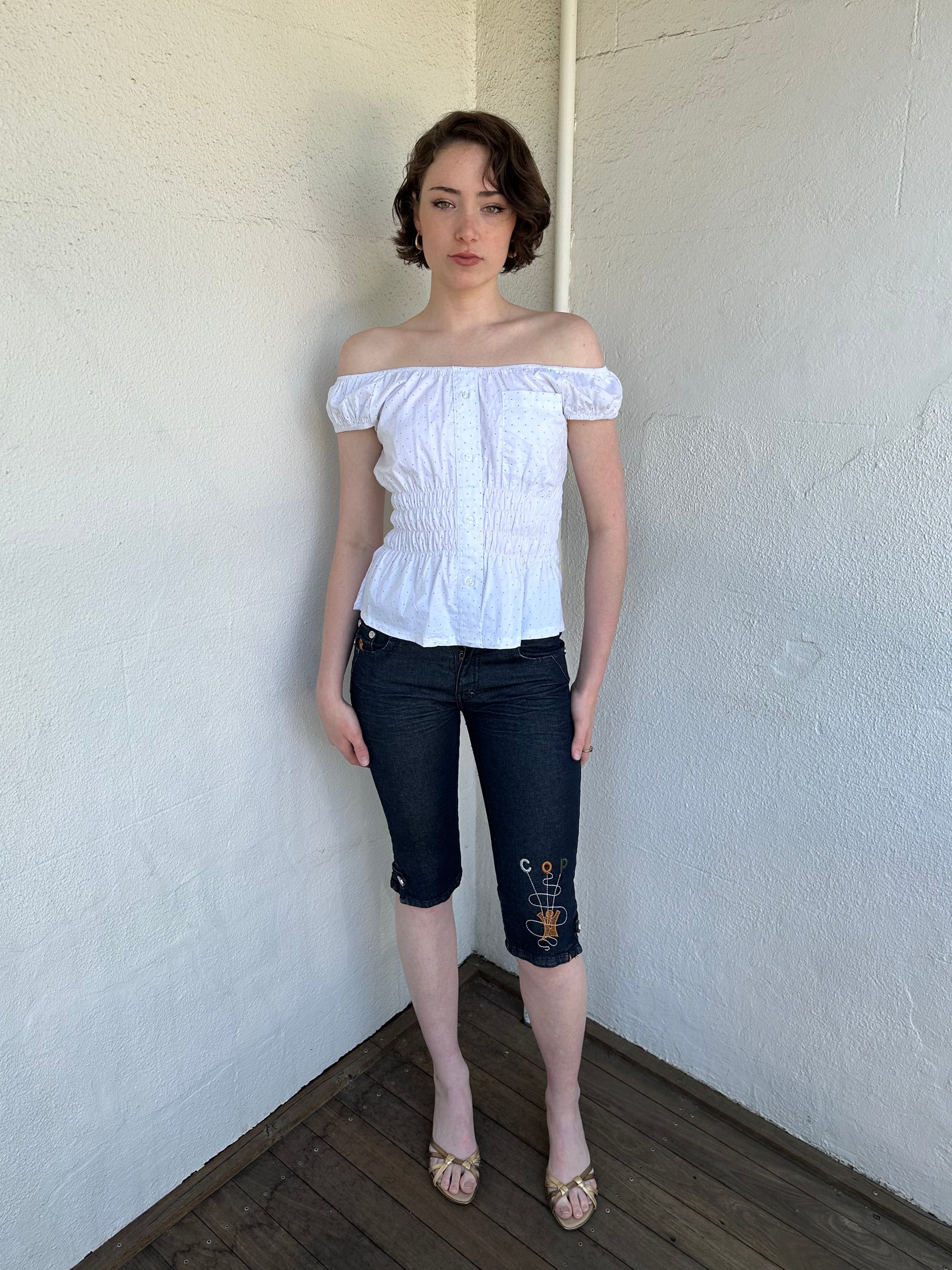Woman Dressed in Y2K Cop Copine embroidered denim capris featuring dark denim with iconic orange and white Cop Copine logo embroidery.