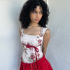 Woman wearing a Y2K 00s cream and red floral mesh tank, with an asymmetric hem and a red underbust ribbon finished with a bow. 