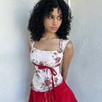 Woman wearing a Y2K 00s cream and red floral mesh tank, with an asymmetric hem and a red underbust ribbon finished with a bow. 
