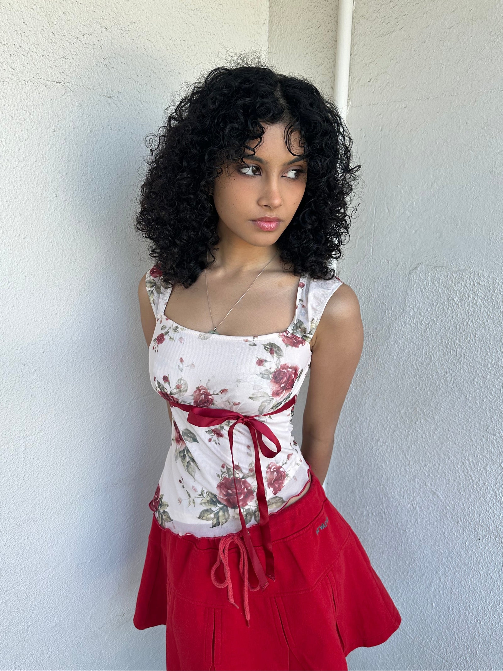 Woman wearing a Y2K 00s cream and red floral mesh tank, with an asymmetric hem and a red underbust ribbon finished with a bow. 