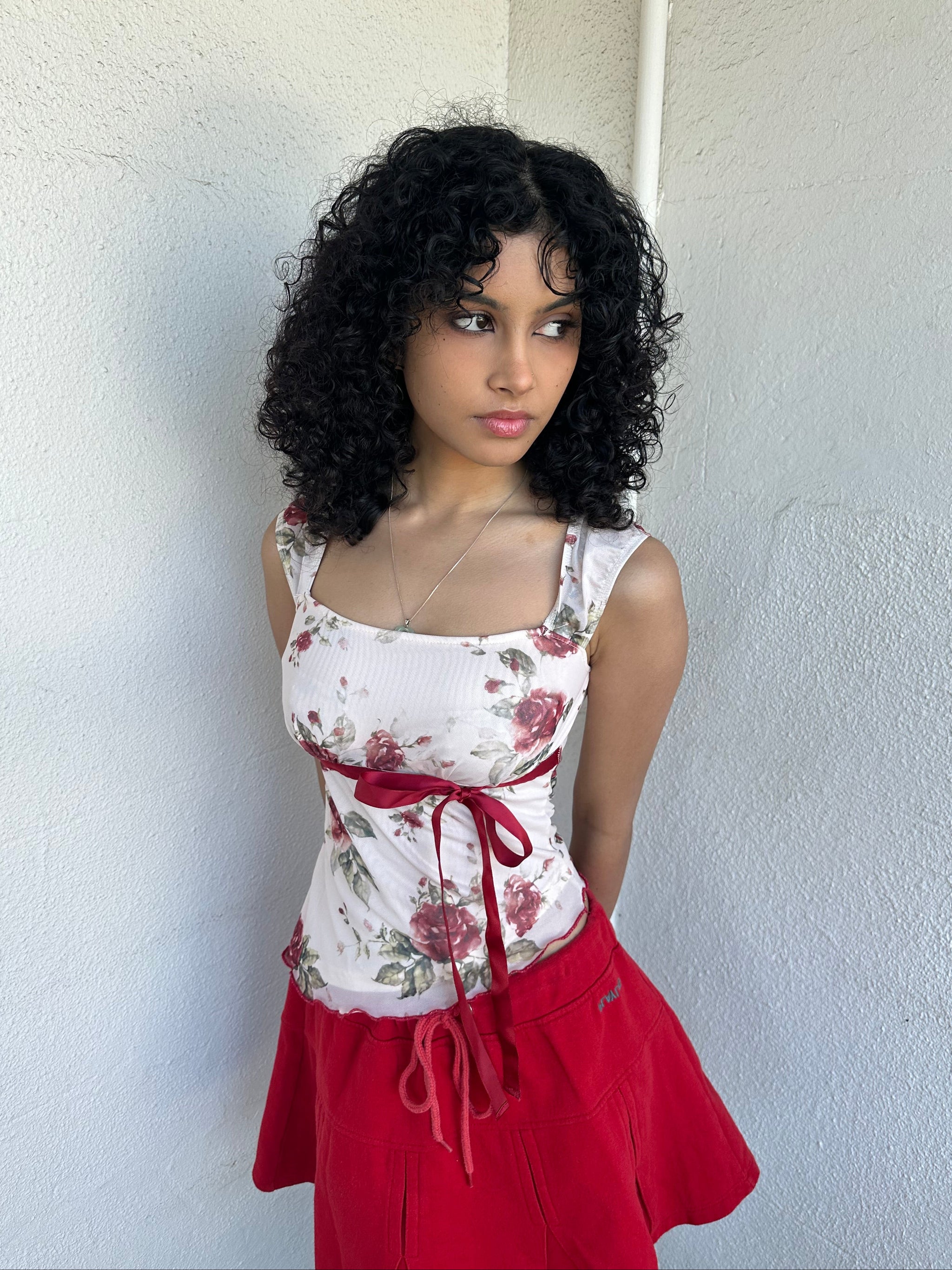 Woman wearing a Y2K 00s cream and red floral mesh tank, with an asymmetric hem and a red underbust ribbon finished with a bow. 