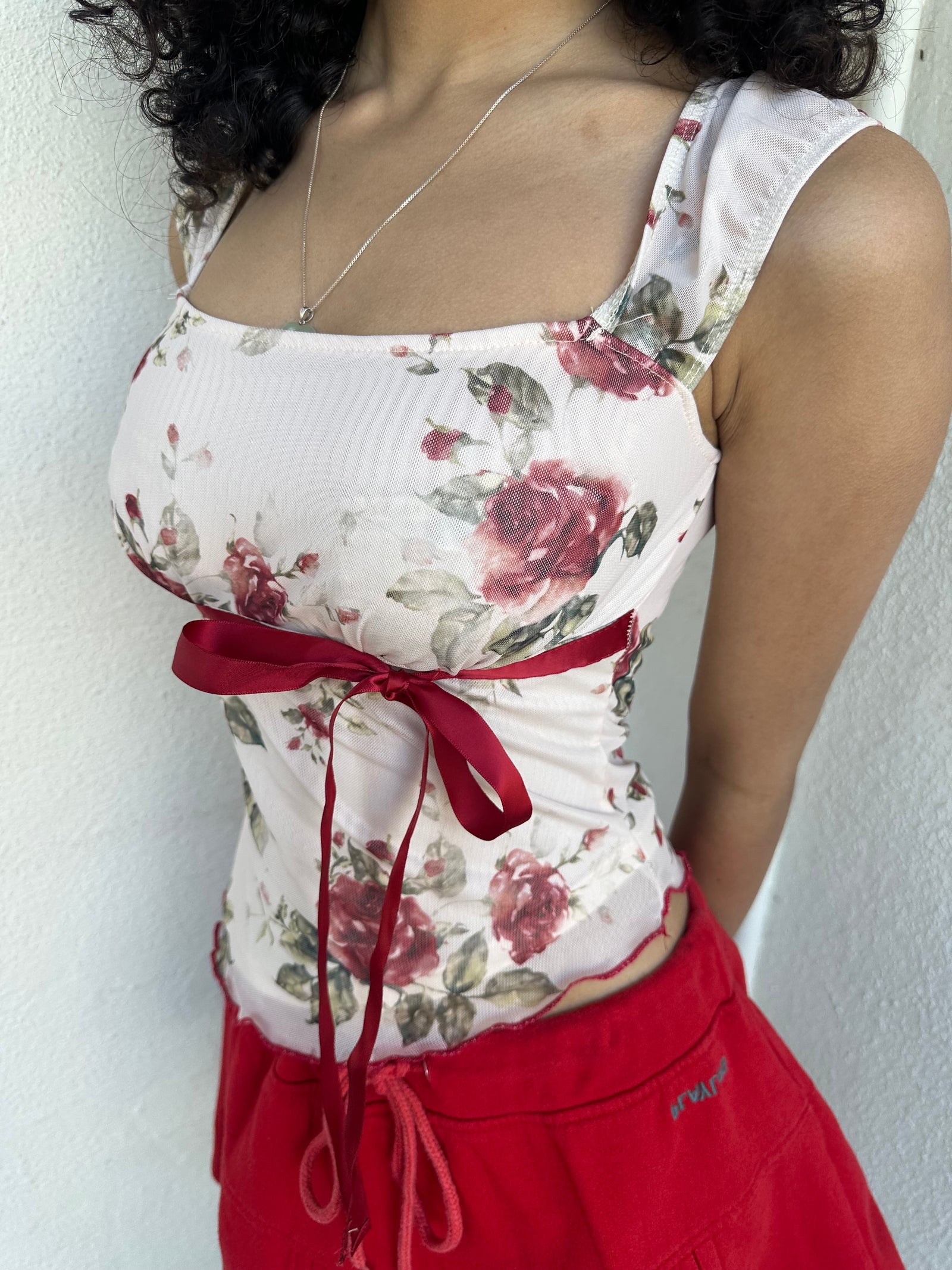 Woman wearing a Y2K 00s cream and red floral mesh tank, with an asymmetric hem and a red underbust ribbon finished with a bow.