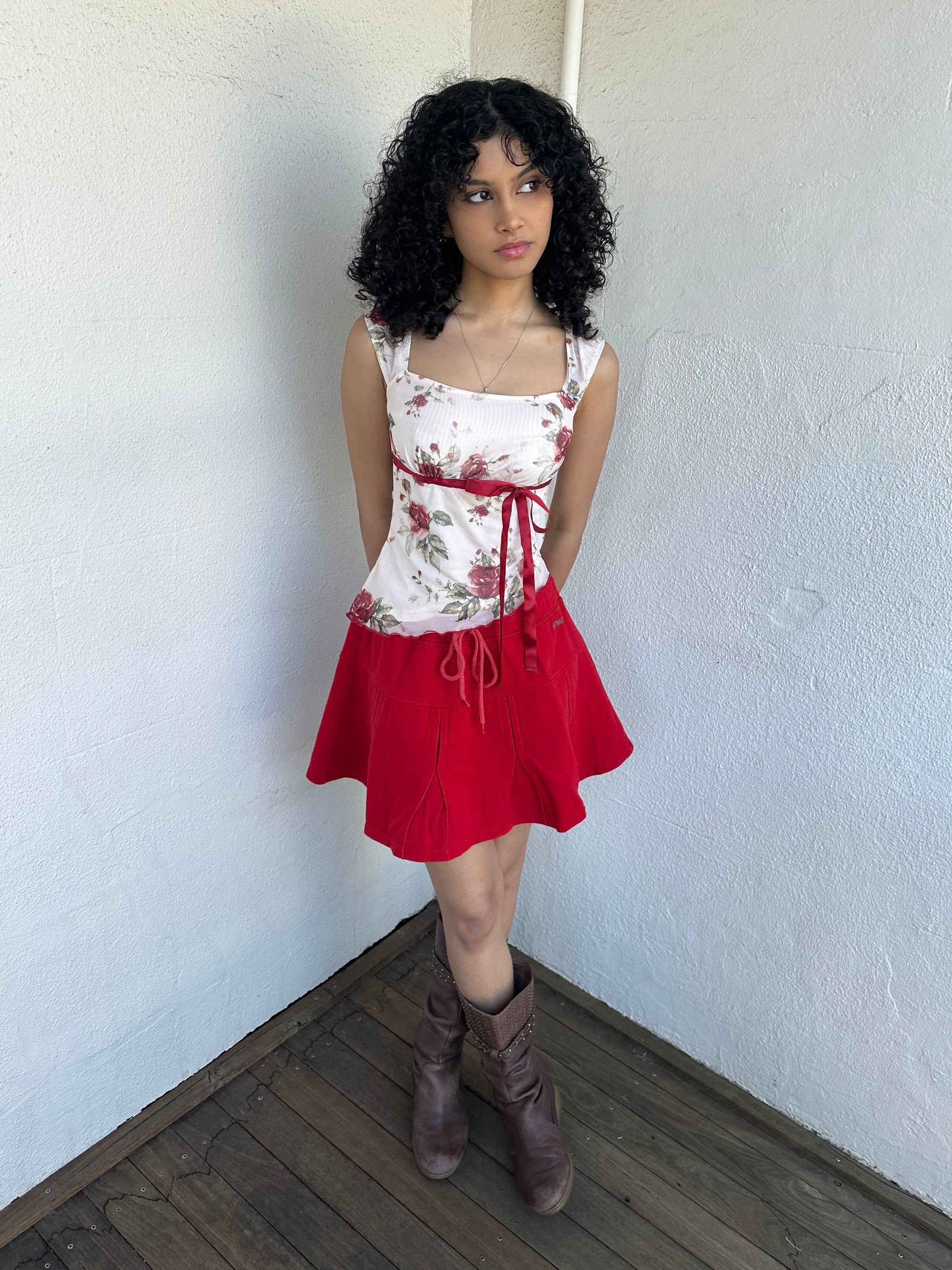 Woman wearing a Y2K 00s cream and red floral mesh tank, with an asymmetric hem and a red underbust ribbon finished with a bow. 