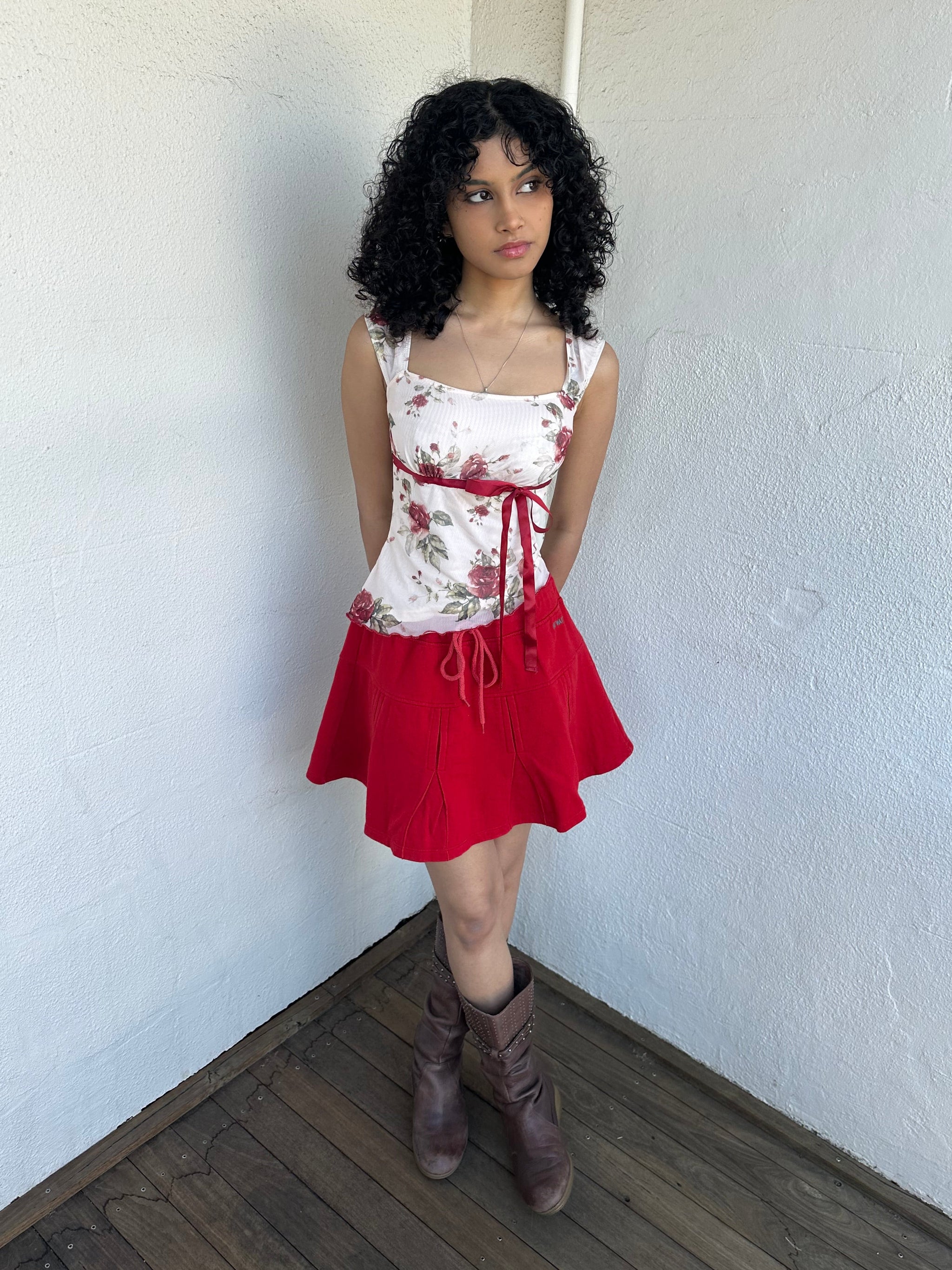 Woman wearing a Y2K 00s cream and red floral mesh tank, with an asymmetric hem and a red underbust ribbon finished with a bow. 