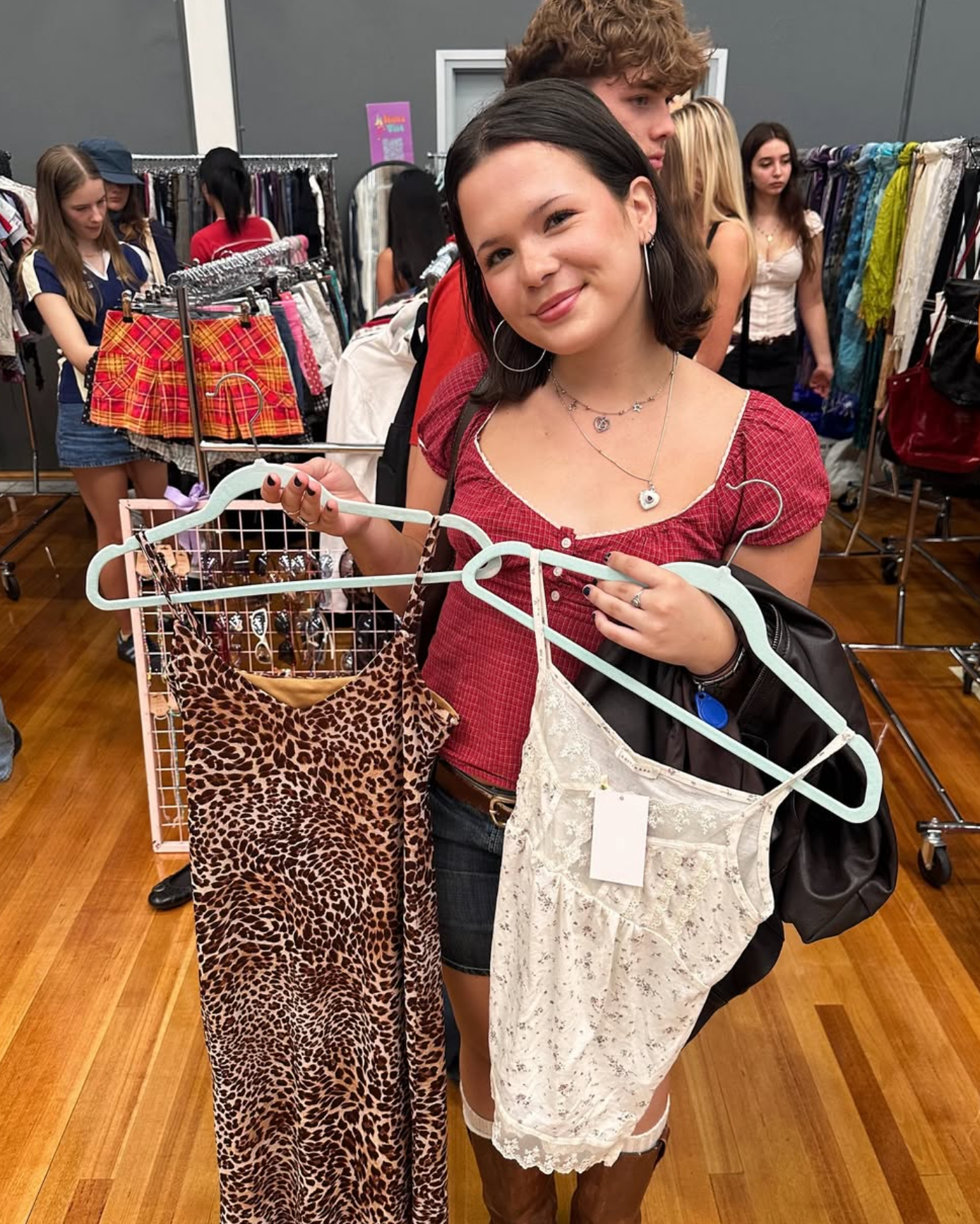 Woman holding a leopard print dress and a white lace garment in market settings