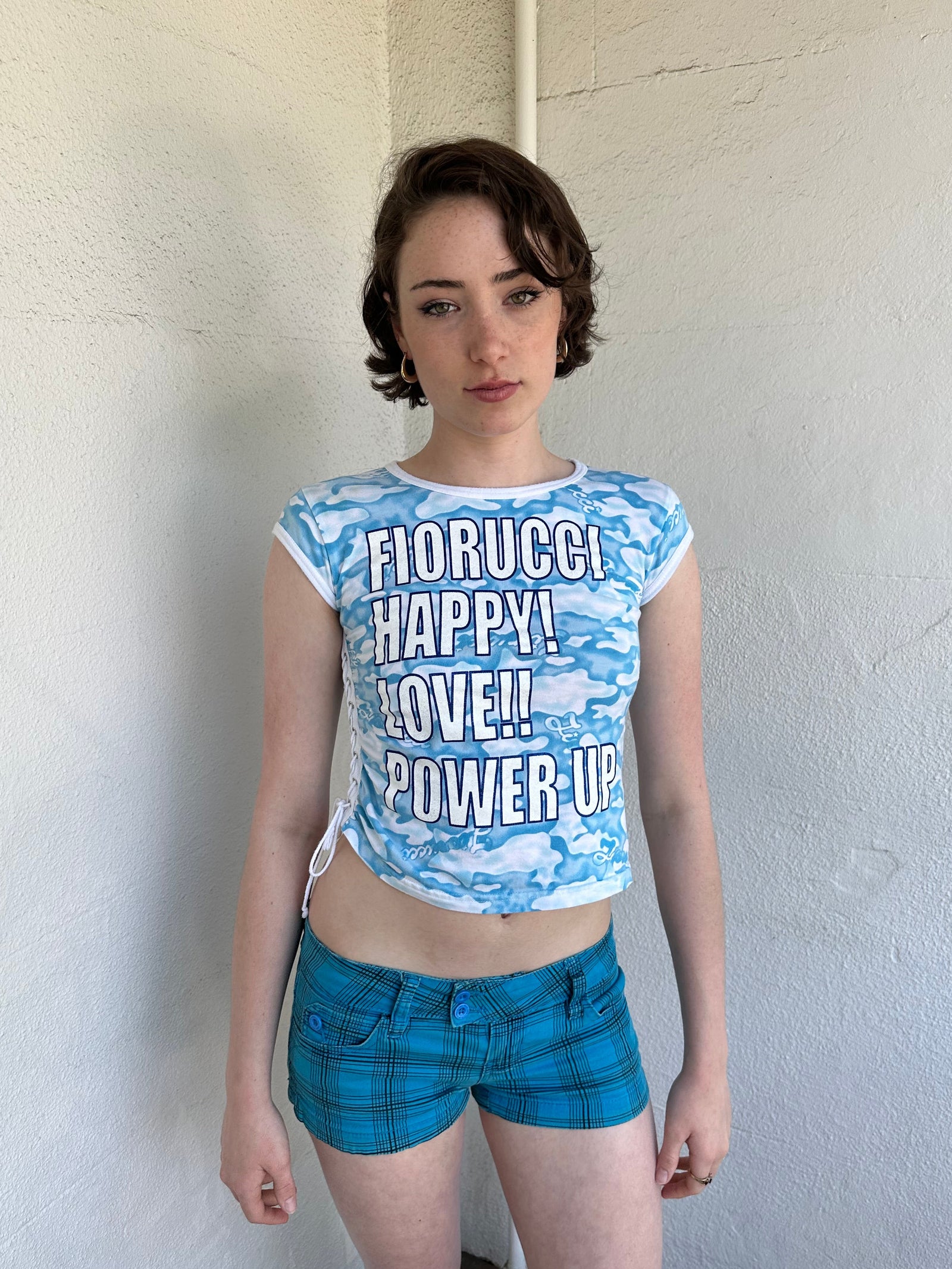 Woman Dressed in Y2K 2000s Fiorucci blue cloud graphic t-shirt featuring a cloud graphic background with large spell-out text 