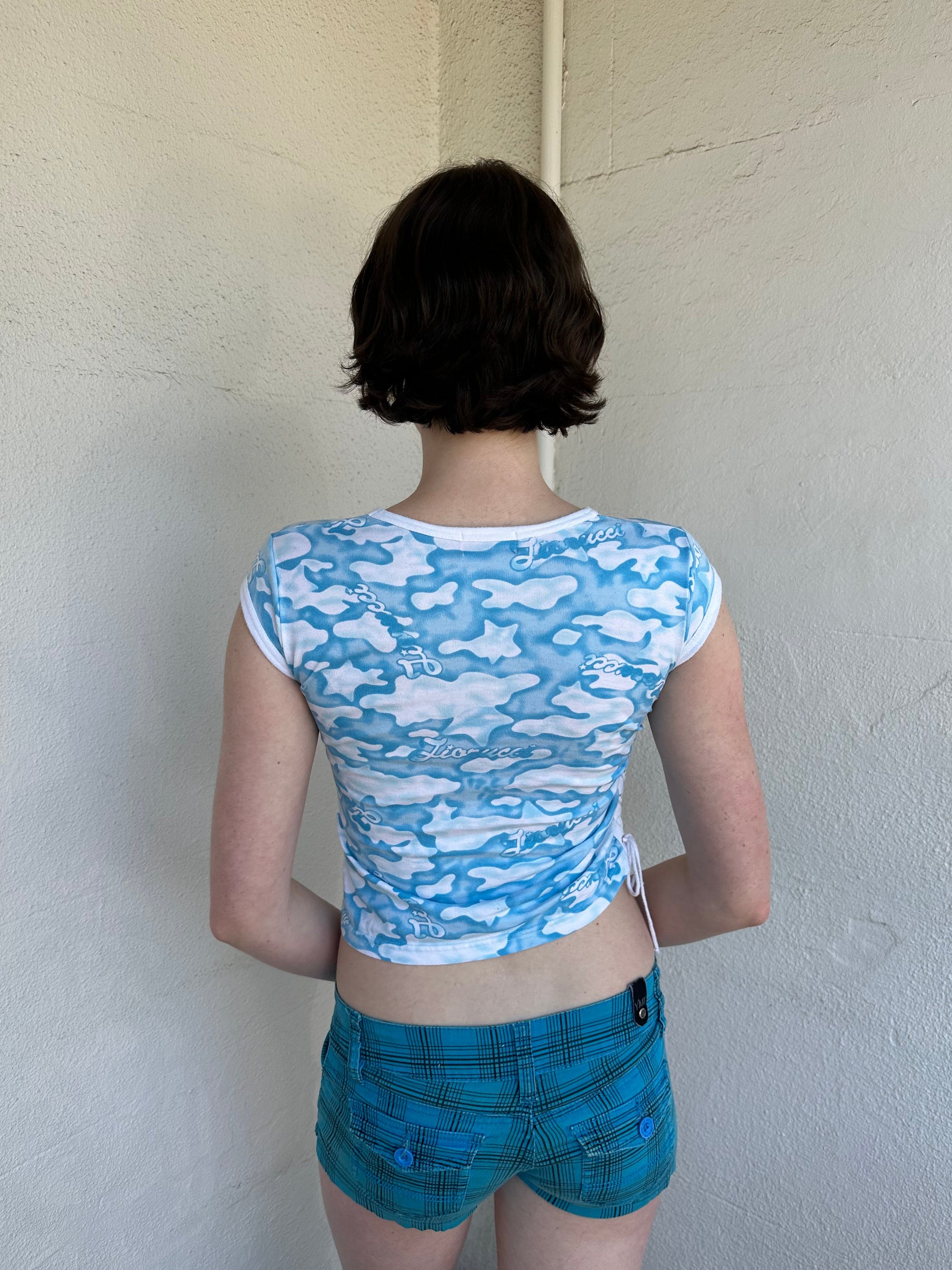 Woman Dressed in Y2K 2000s Fiorucci blue cloud graphic t-shirt featuring a cloud graphic background with large spell-out text 
