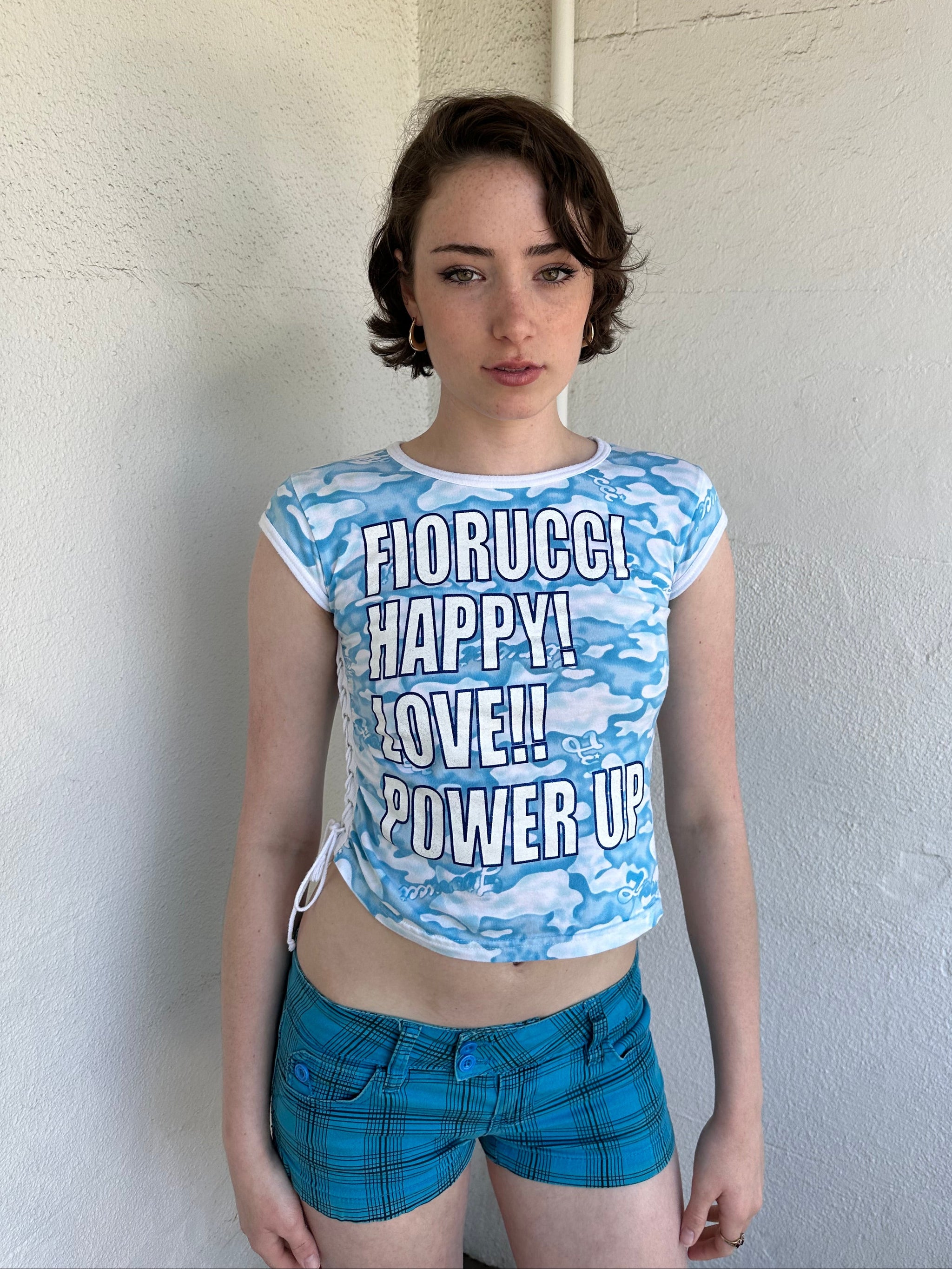 Woman Dressed in Y2K 2000s Fiorucci blue cloud graphic t-shirt featuring a cloud graphic background with large spell-out text 