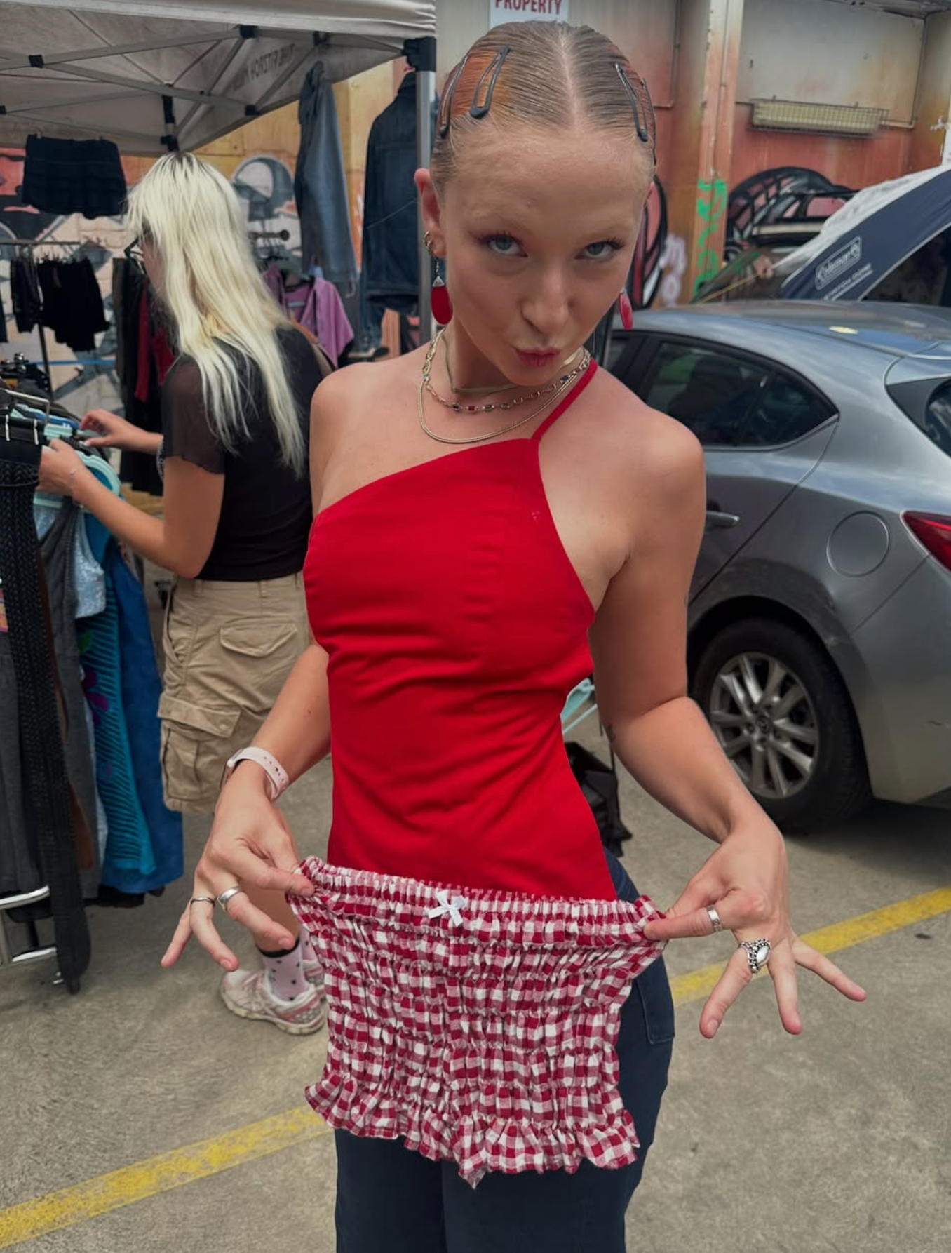 Woman in a red top holding up a checkered skirt in an outdoor setting