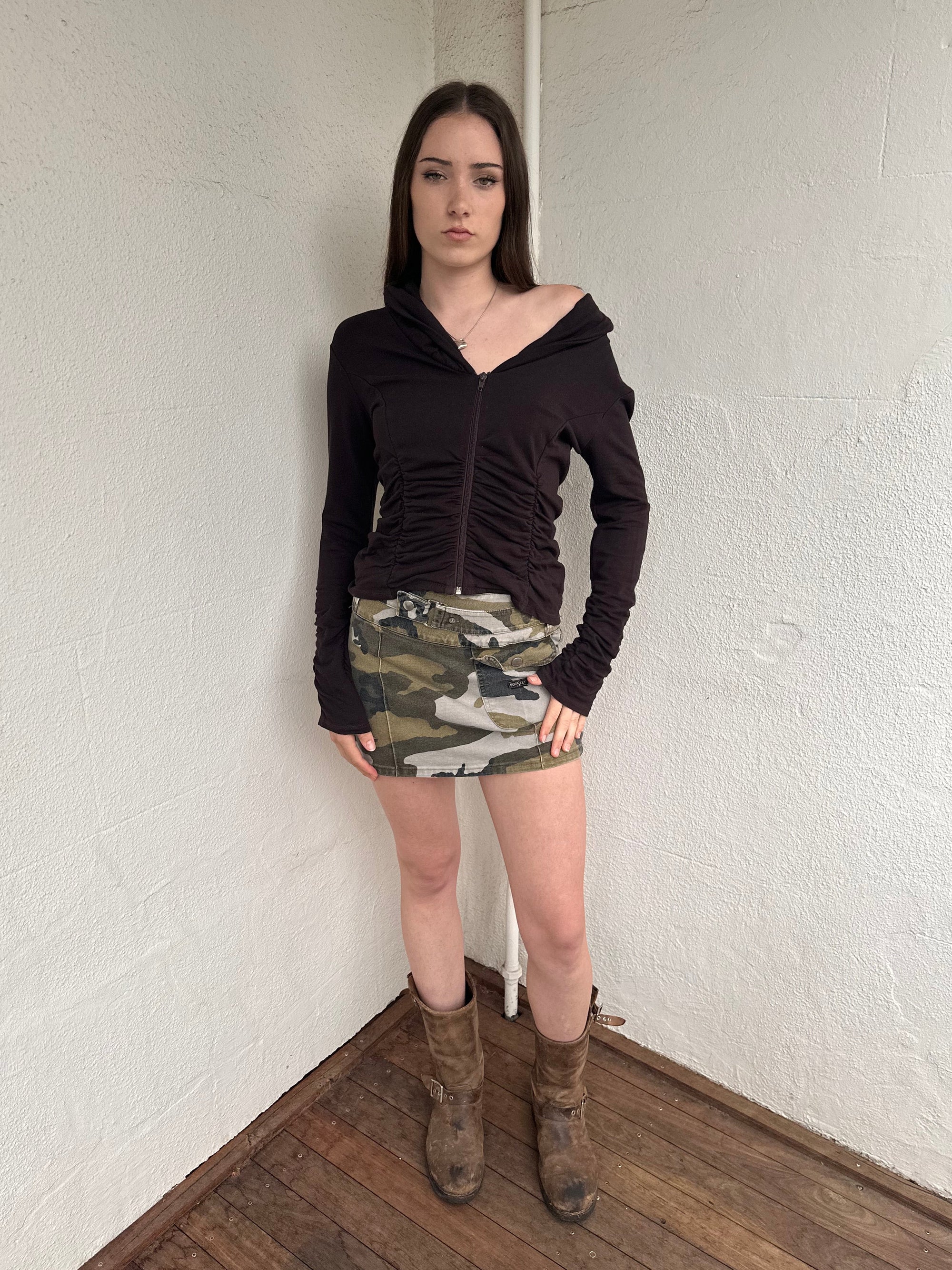 Women wearing a 00s Y2K Green camo denim mini skirt with a built-in belt. Crafted from sturdy denim with cargo-style detailing for added texture