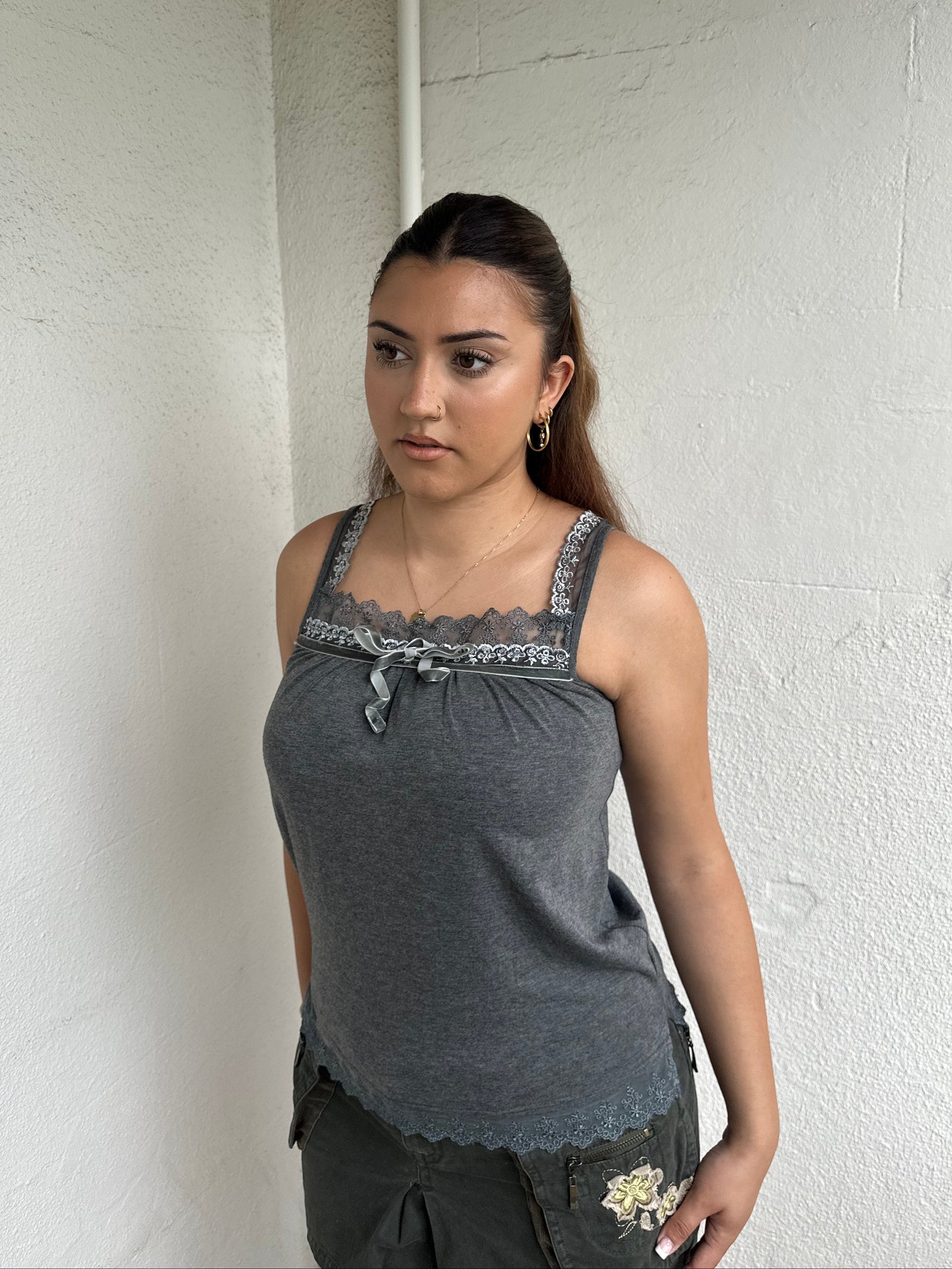 Woman Dressed in Y2K 00s Grey lace trimmed cami featuring a soft grey jersey material with lace trim along the neckline. 