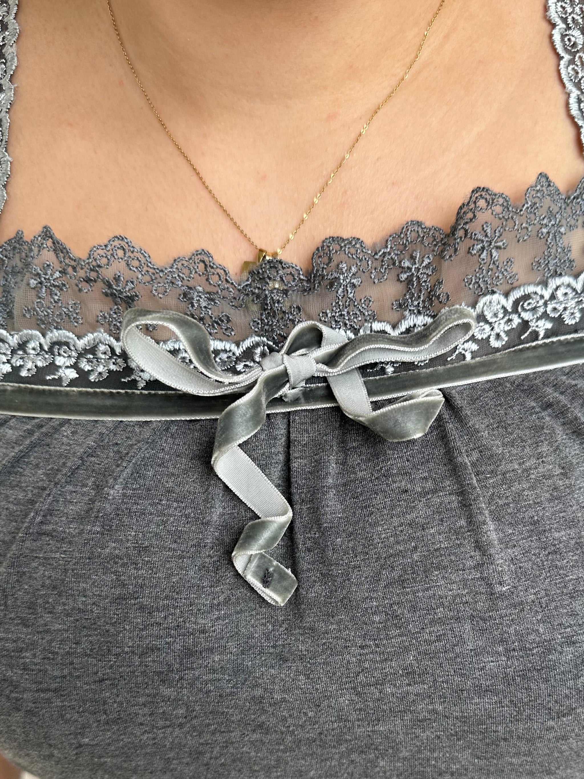 Woman Dressed in Y2K 00s Grey lace trimmed cami featuring a soft grey jersey material with lace trim along the neckline. 