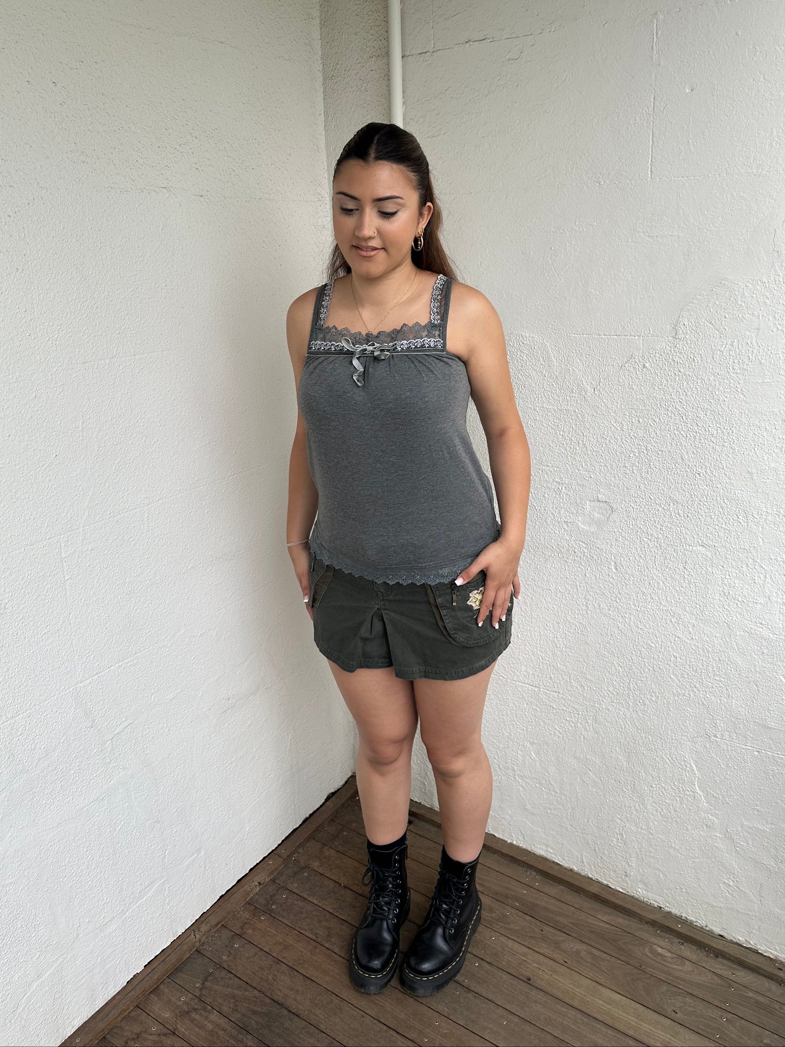 Woman Dressed in Y2K 00s Grey lace trimmed cami featuring a soft grey jersey material with lace trim along the neckline. 