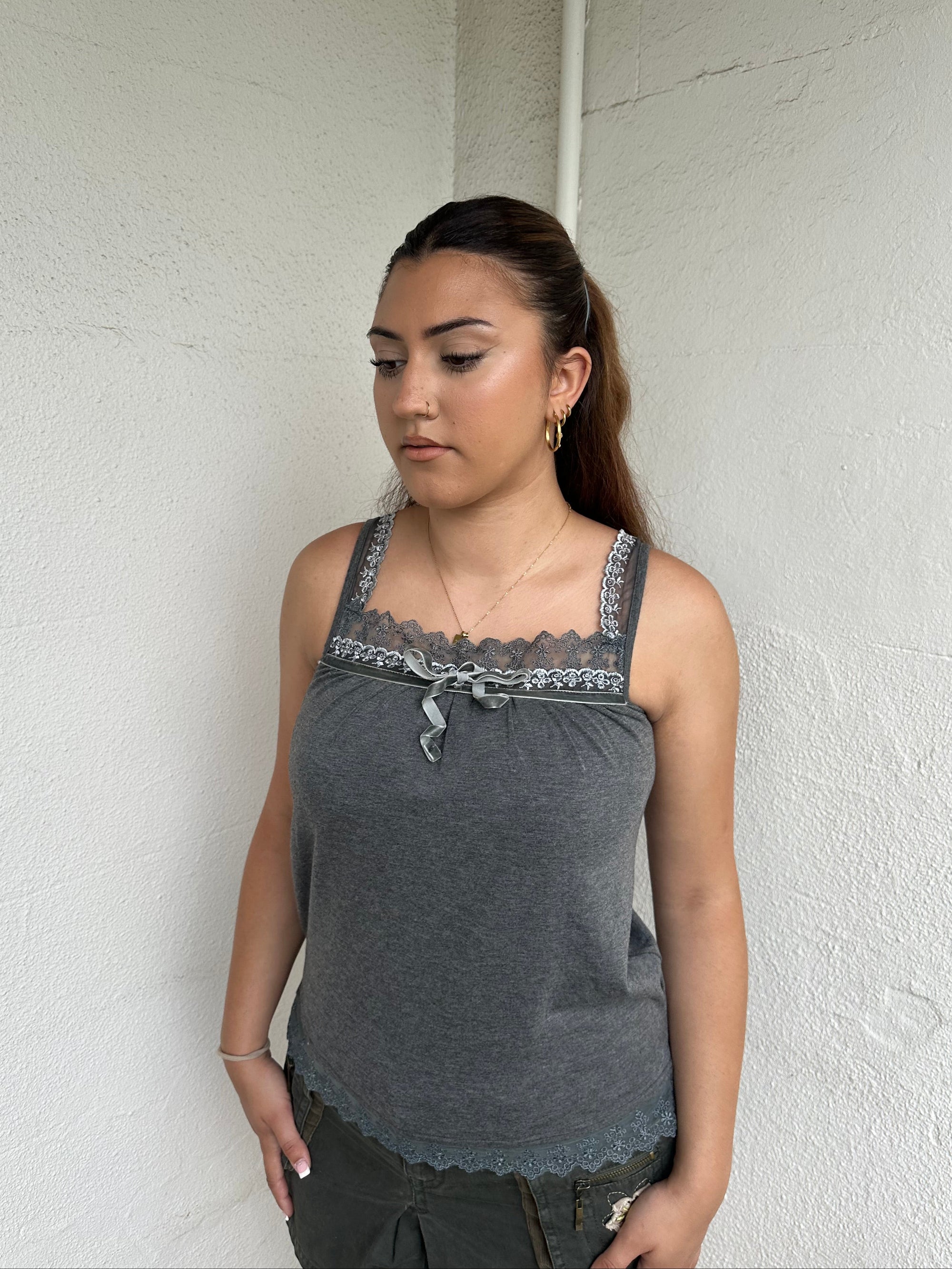 Woman Dressed in Y2K 00s Grey lace trimmed cami featuring a soft grey jersey material with lace trim along the neckline. 
