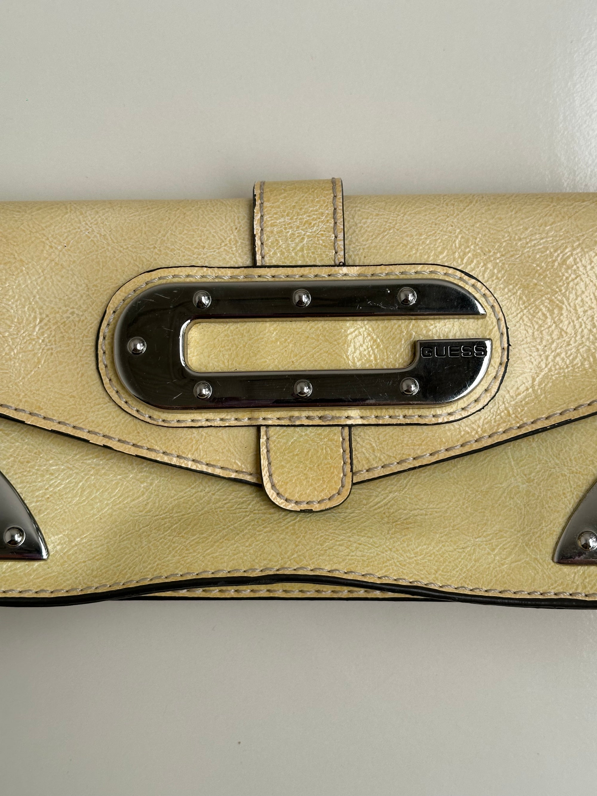 guess-pastel-yellow-mini-shoulder-bagWomen wearing a 00s Y2K Guess pastel yellow mini shoulder bag from the 2000s crafted from faux leather in a small rectangular shape.