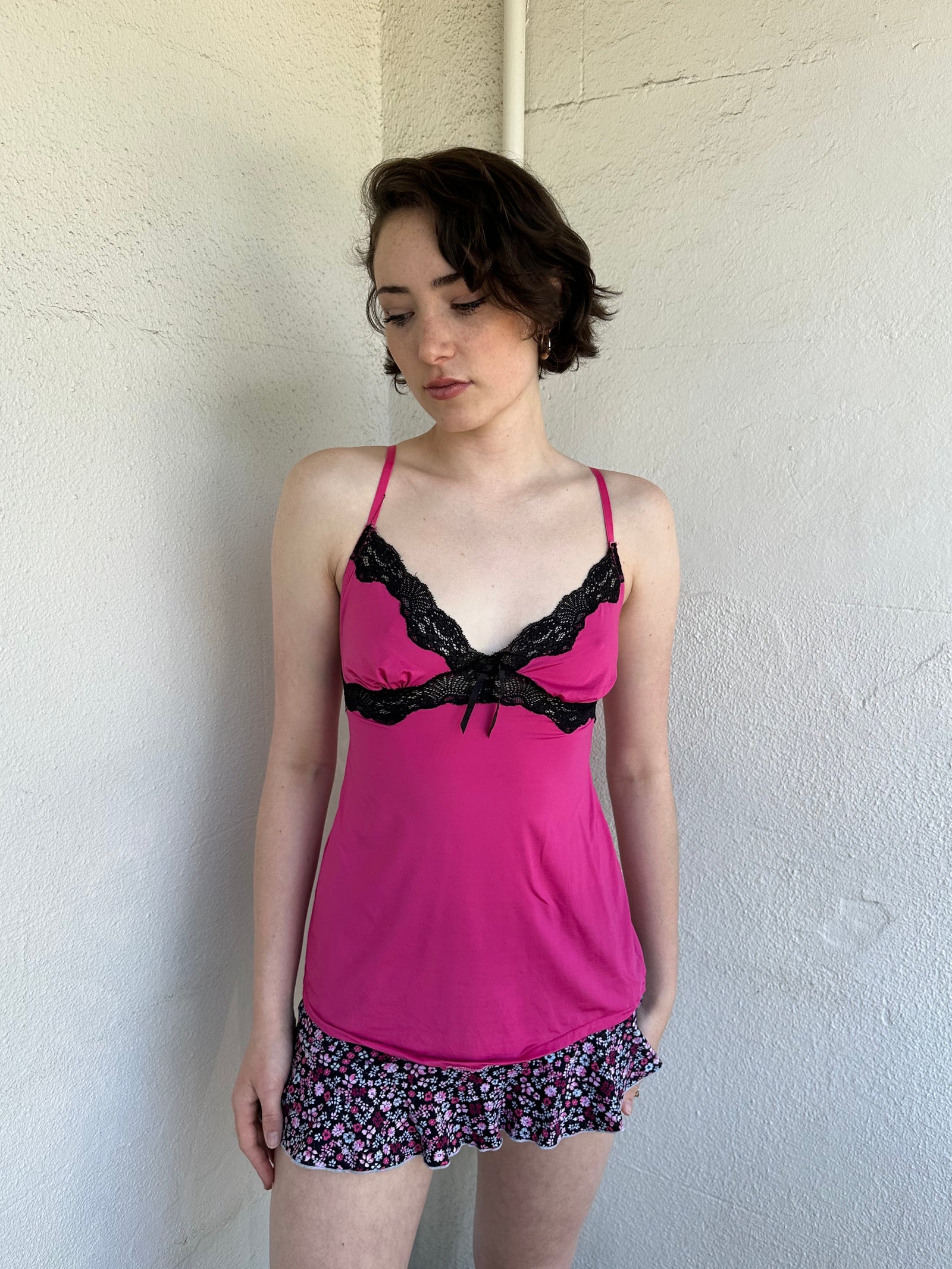 Woman Dressed in Y2K Hot pink and black lace trim cami top featuring a stretchy hot pink fabric body with black lace detailing across the bust.