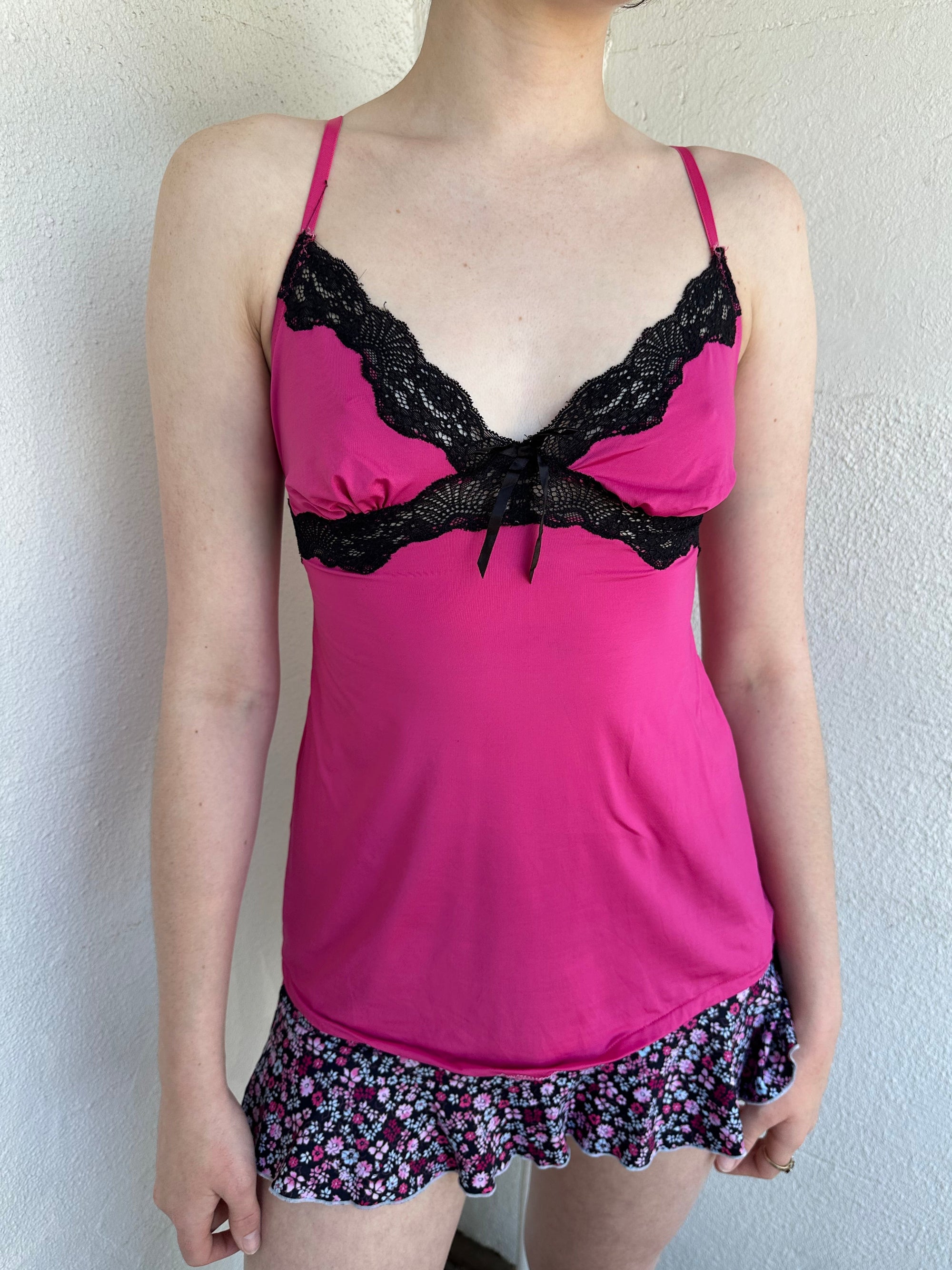 Woman Dressed in Y2K Hot pink and black lace trim cami top featuring a stretchy hot pink fabric body with black lace detailing across the bust.
