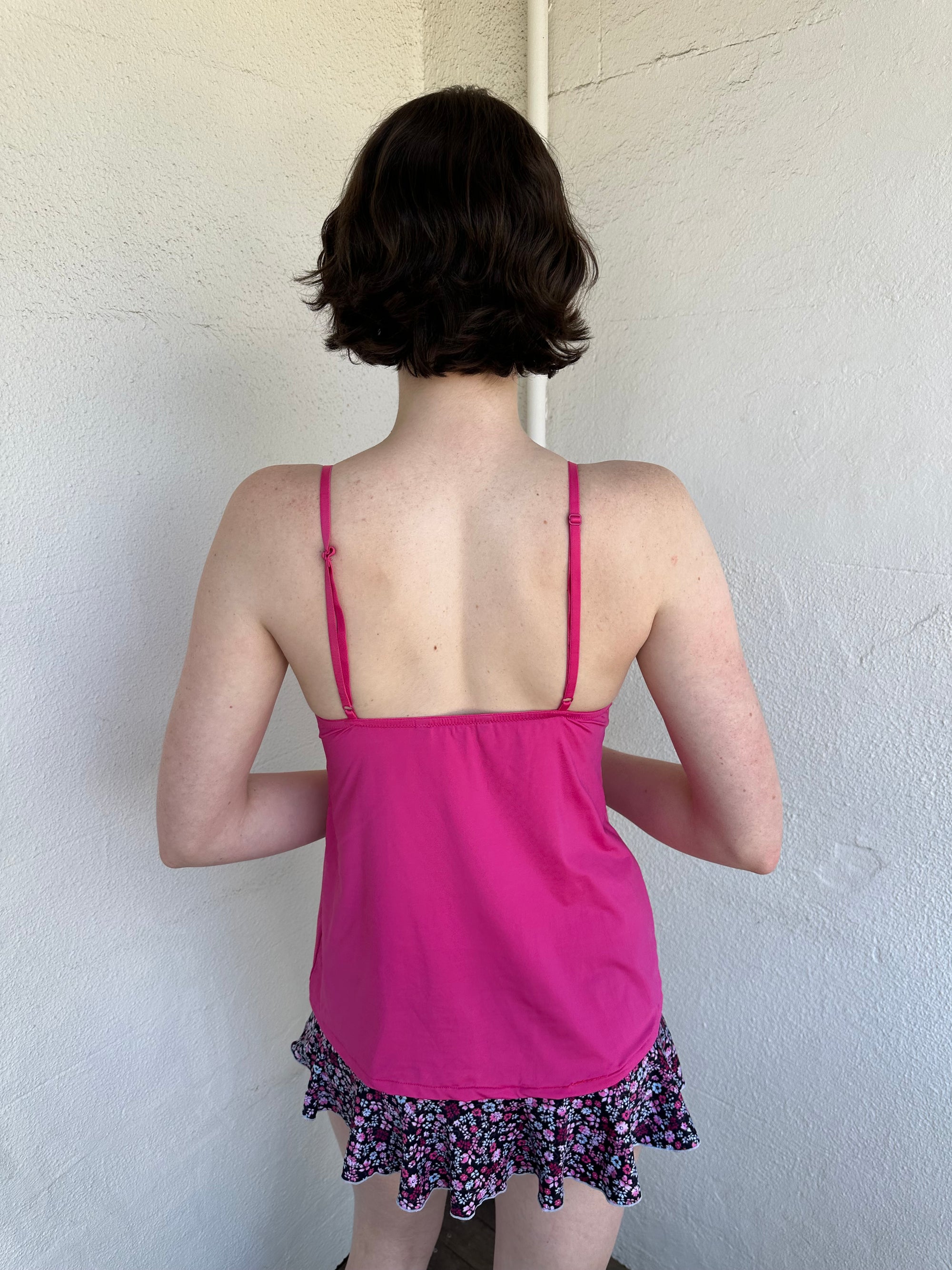 Woman Dressed in Y2K Hot pink and black lace trim cami top featuring a stretchy hot pink fabric body with black lace detailing across the bust.