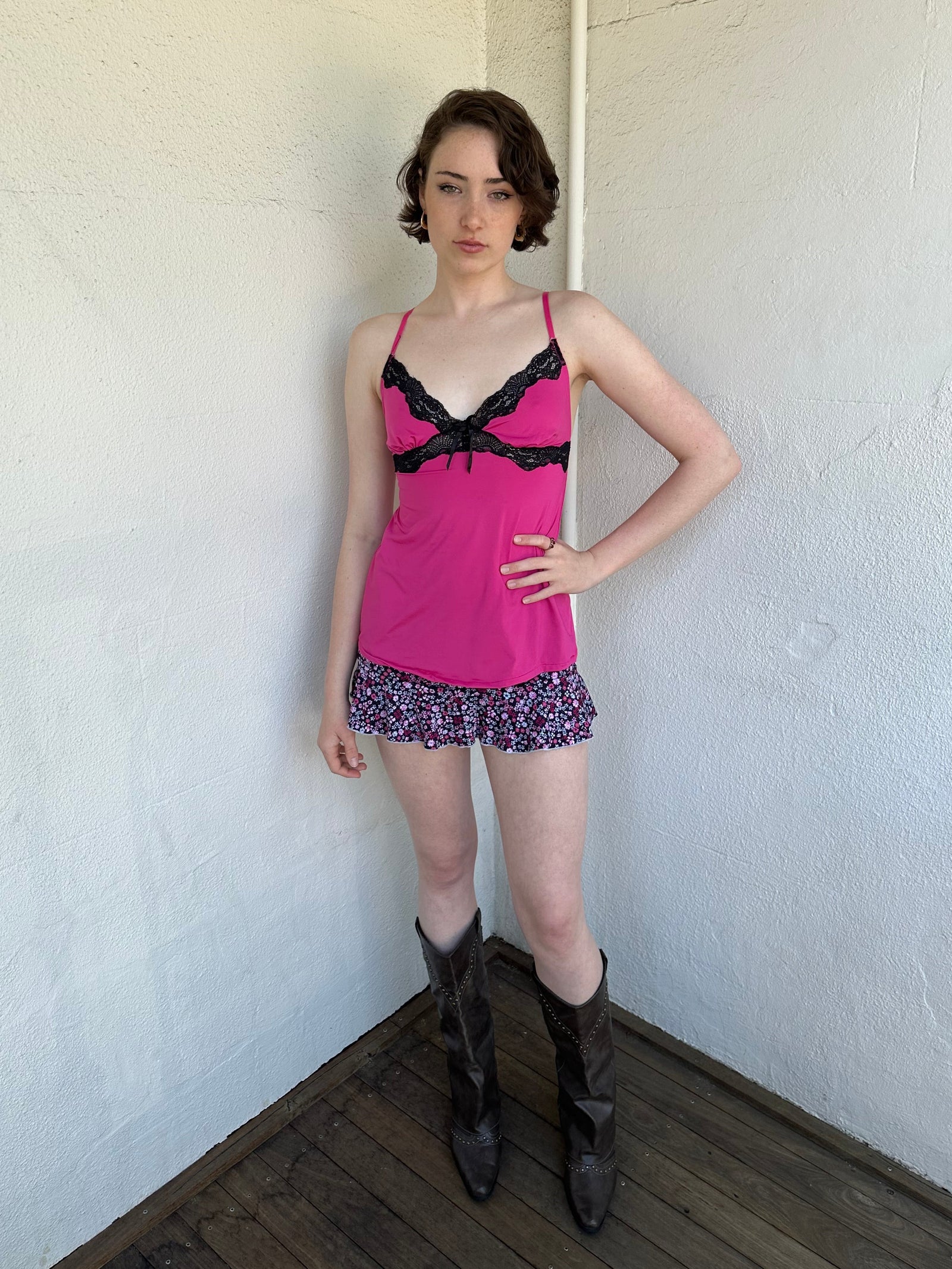 Woman Dressed in Y2K Hot pink and black lace trim cami top featuring a stretchy hot pink fabric body with black lace detailing across the bust.