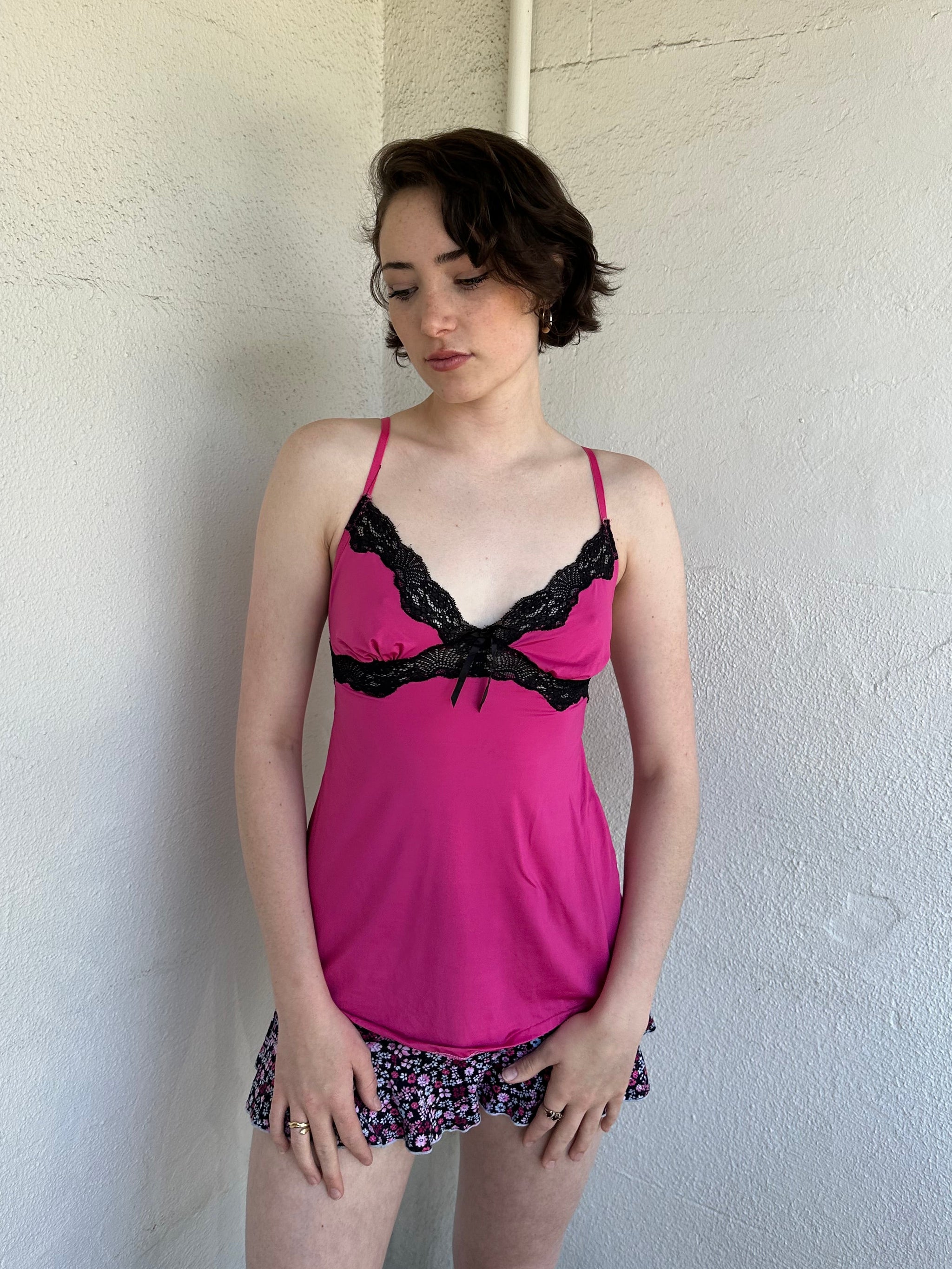 Woman Dressed in Y2K Hot pink and black lace trim cami top featuring a stretchy hot pink fabric body with black lace detailing across the bust.