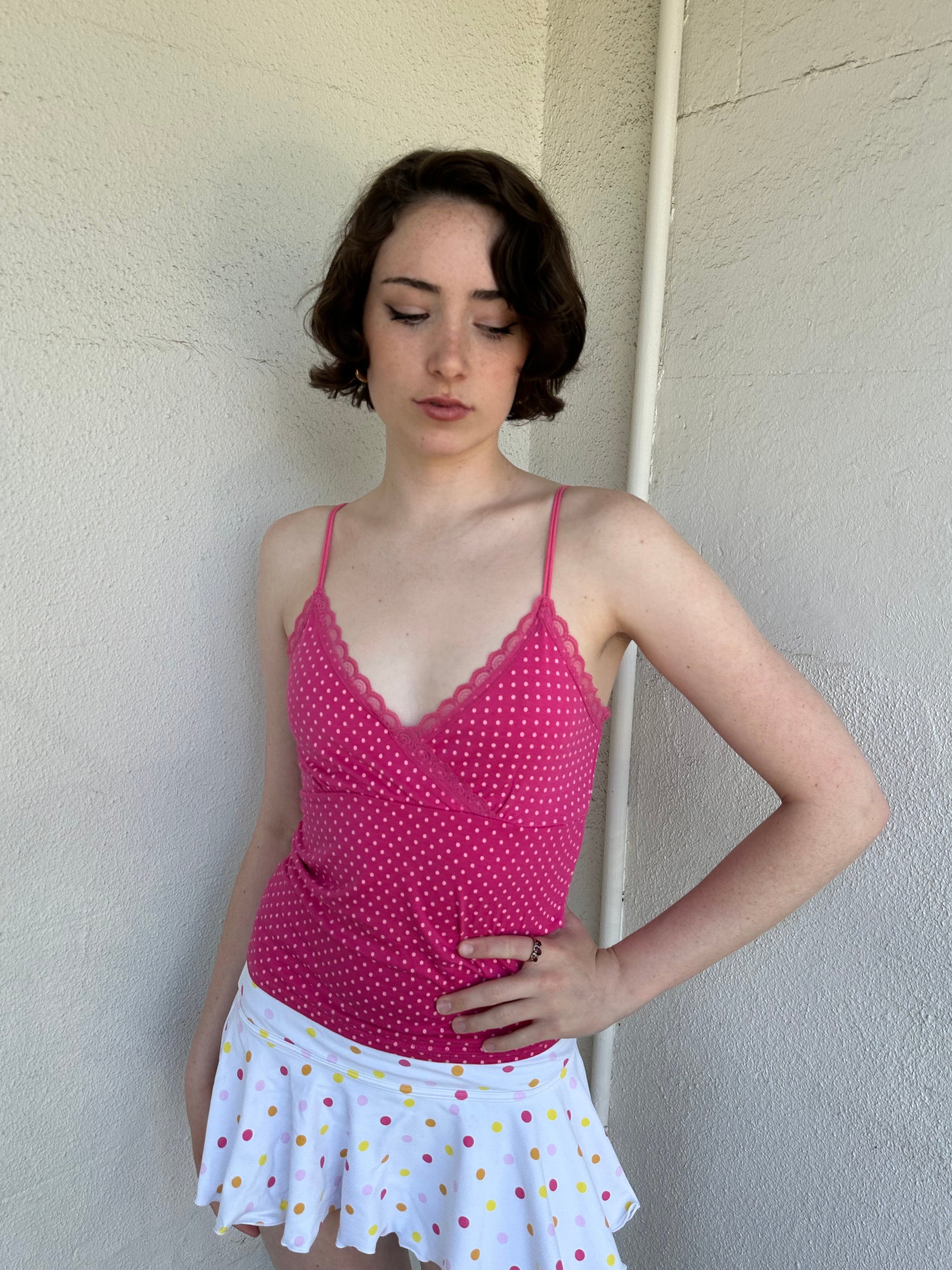 Woman Dressed in Y2K Hot pink and baby pink polkadot cami top featuring small white polkadots throughout a vibrant hot pink base.
